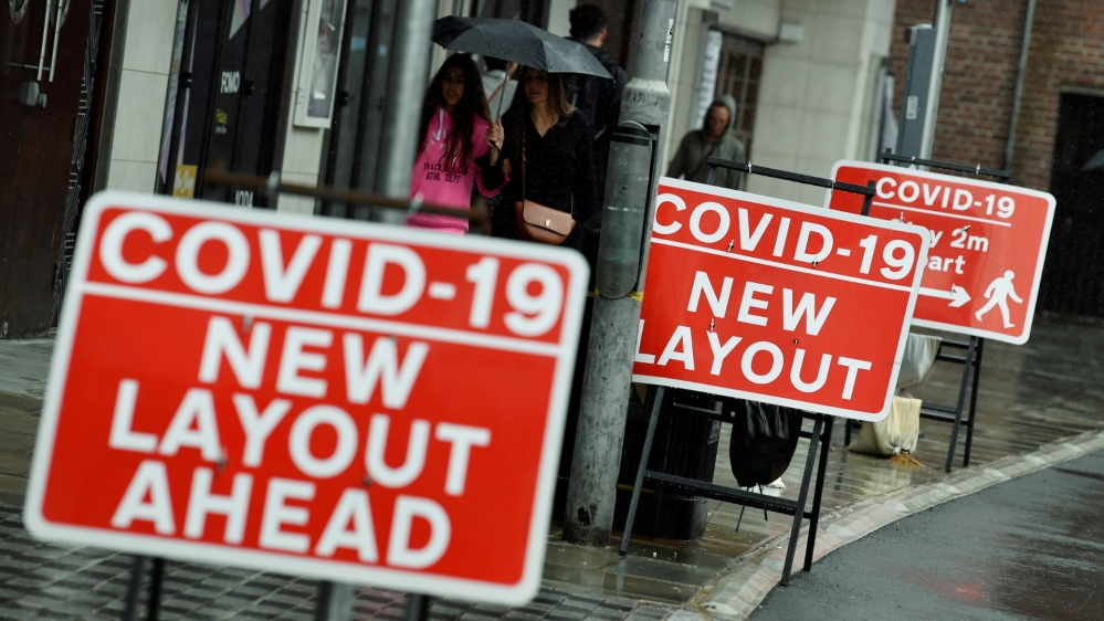 Shoppers walk past social distancing signs following the outbreak of the coronavirus disease, in London