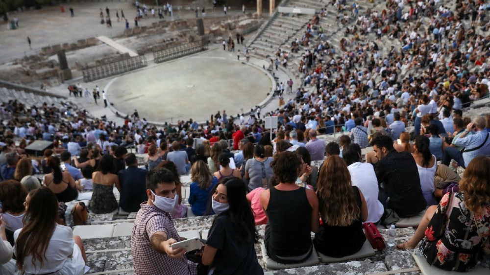 People wearing protective face masks take a selfie as they wait for the start of an ancient Greek drama at the ancient amphitheatre of Epidaurus, Greece