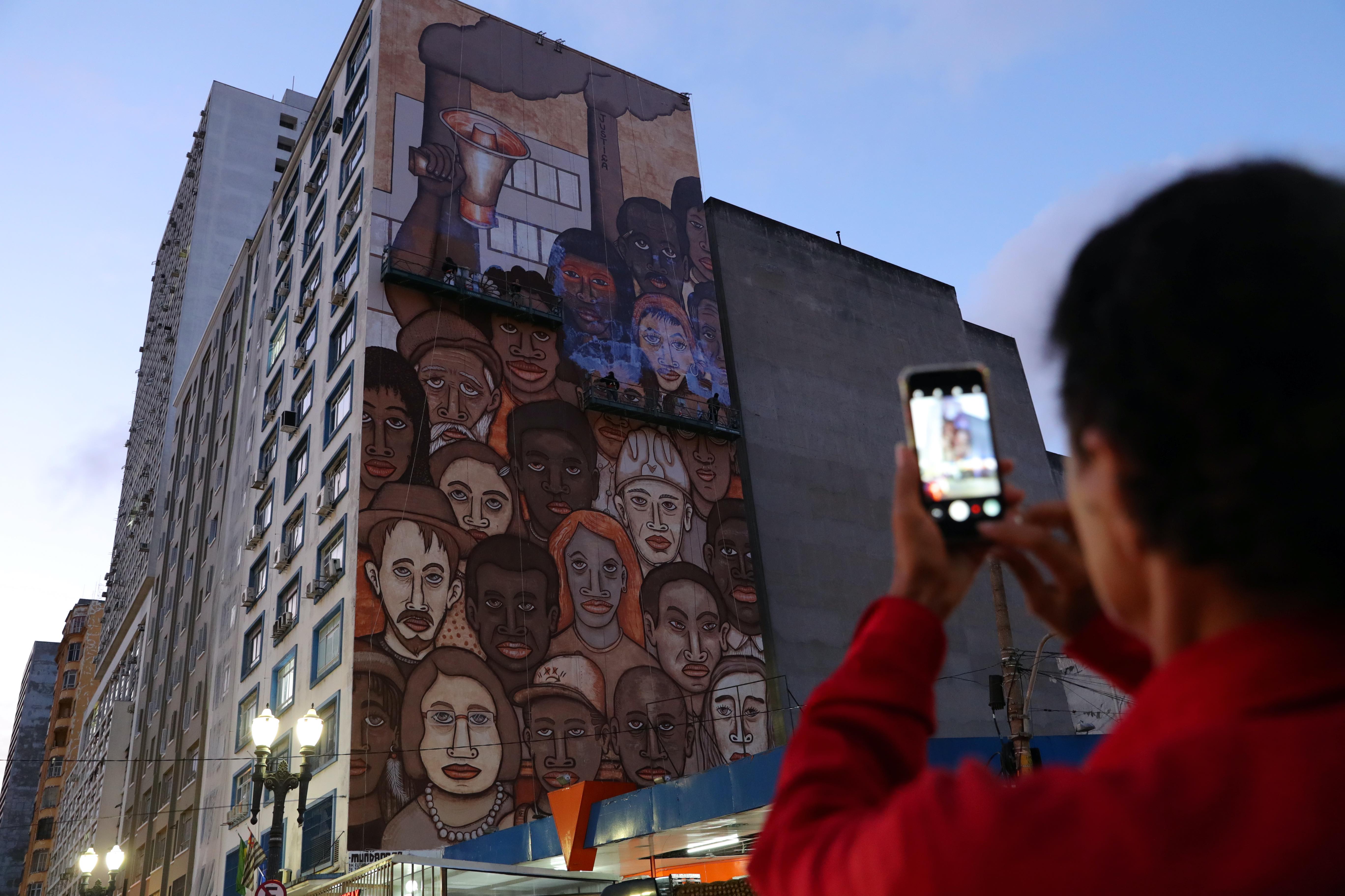 A man takes a picture as Brazilian artist Mundano works on a mural honour victims of the mining disaster, in Sao Paulo, Brazil