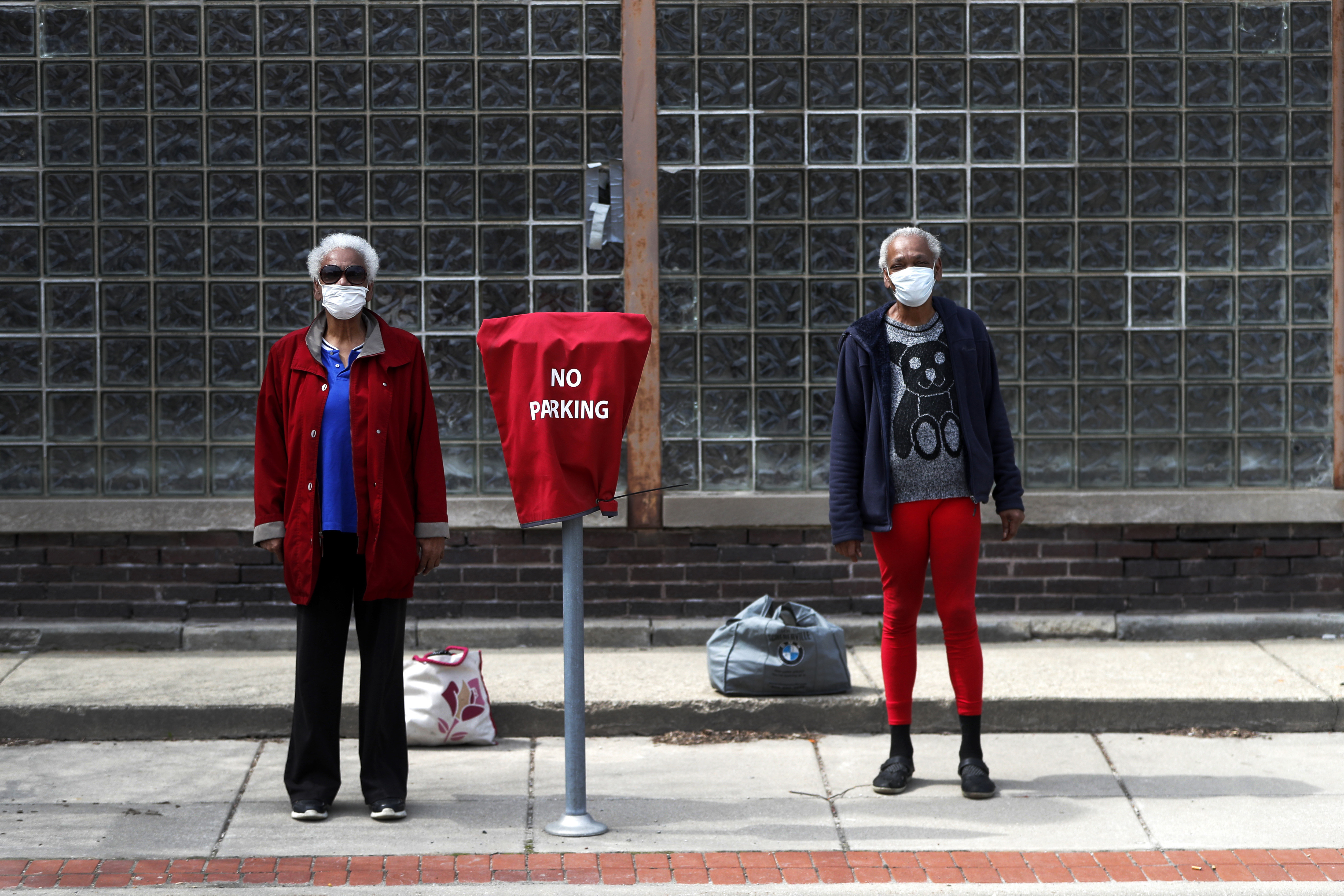 Two women wait for a bus after visiting a friend in the US state of Illinois on April 6, 2020. A disproportionate number of Black people have died of COVID-19 complications in Chicago [File: AP/Charles Rex Arbogast]