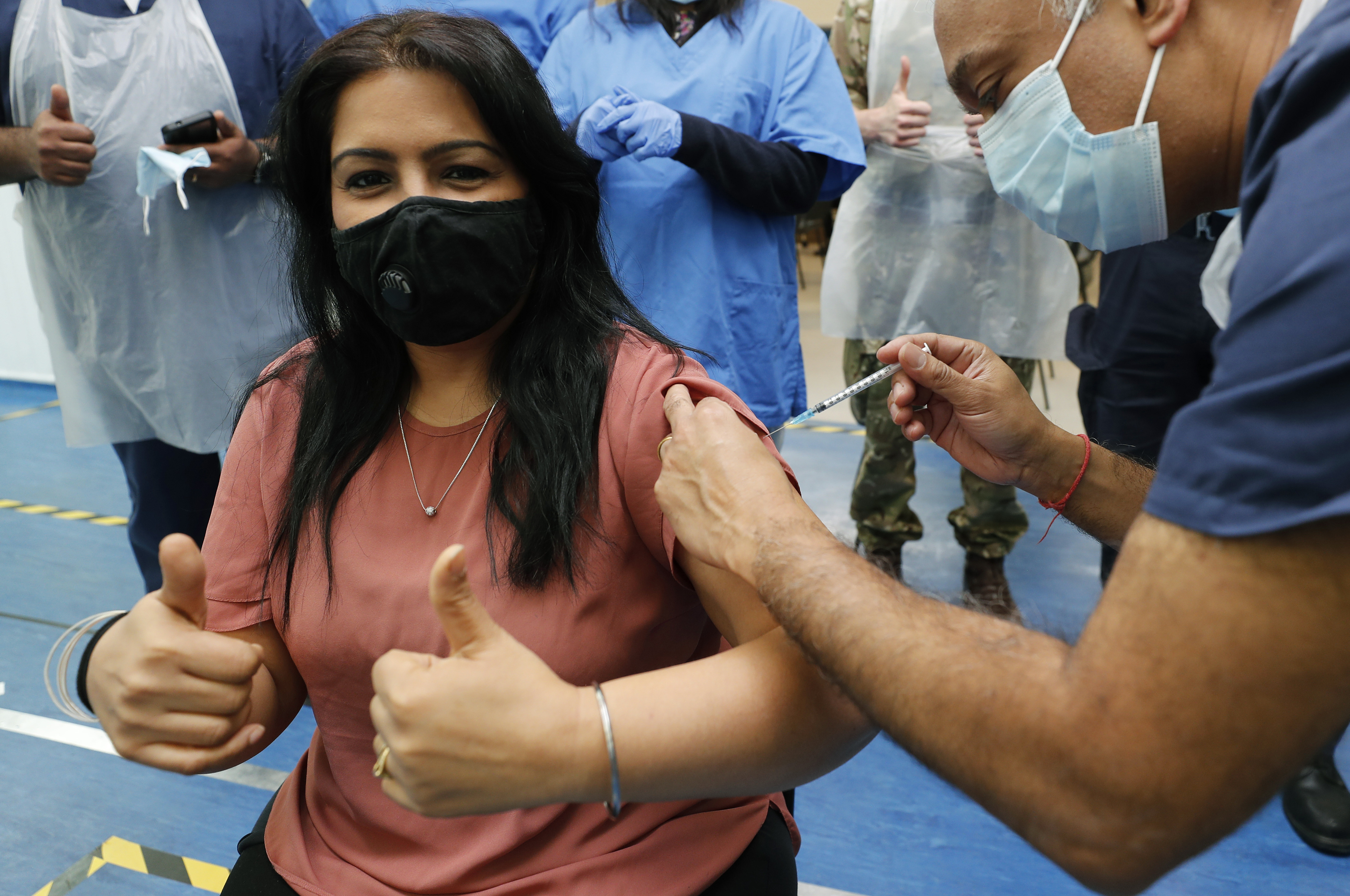 Dr Anil Mehta, surrounded by his team of doctors, administers a dose of the Pfizer vaccine to Geeta Waddon to mark the 10,000th jab in his small practice in London on February 28, 2021 [AP/Frank Augstein]
