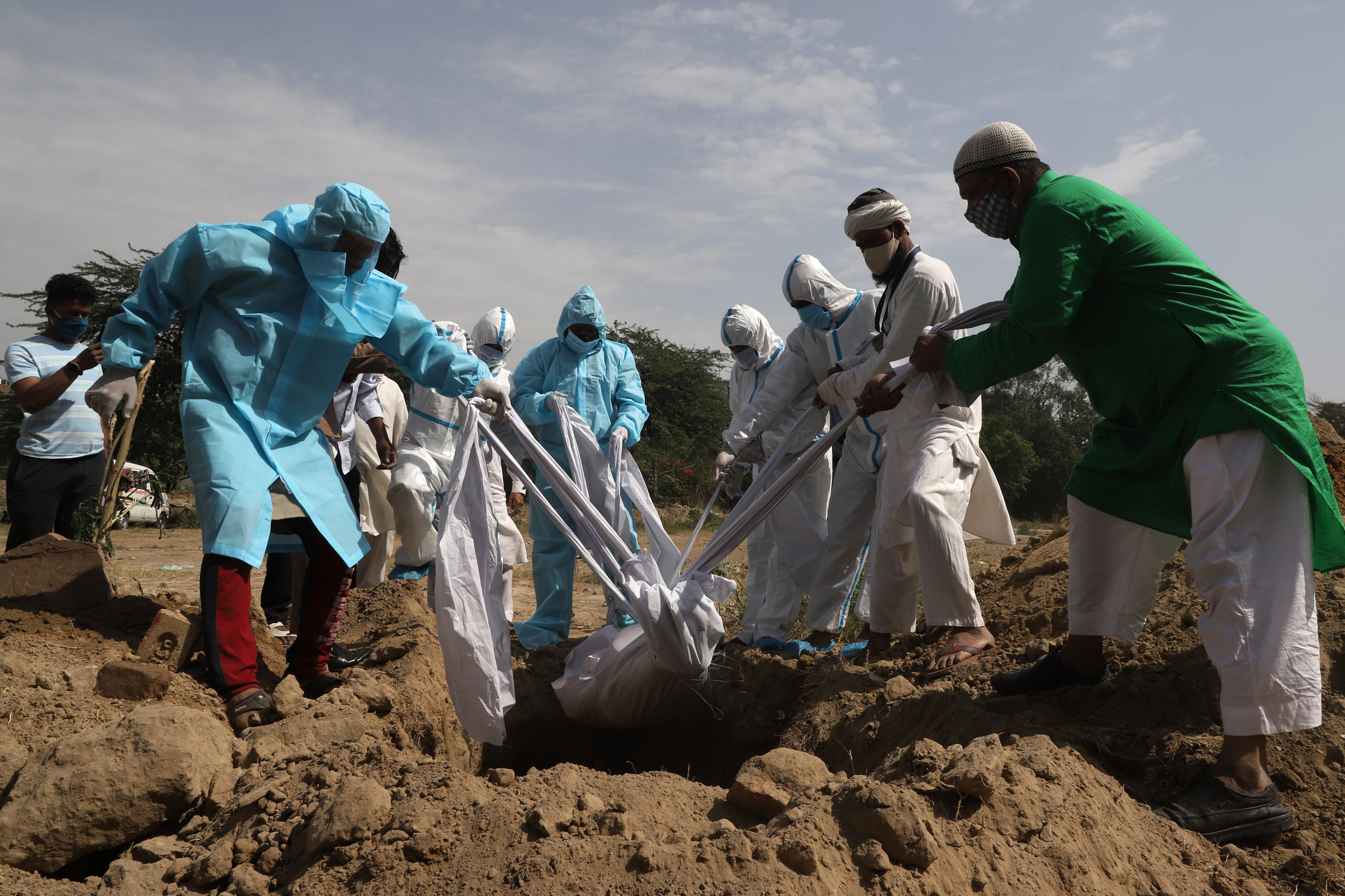 Relatives and health workers bury the body of a man who died of COVID-19 in New Delhi [Bhat Burhan/Al Jazeera]