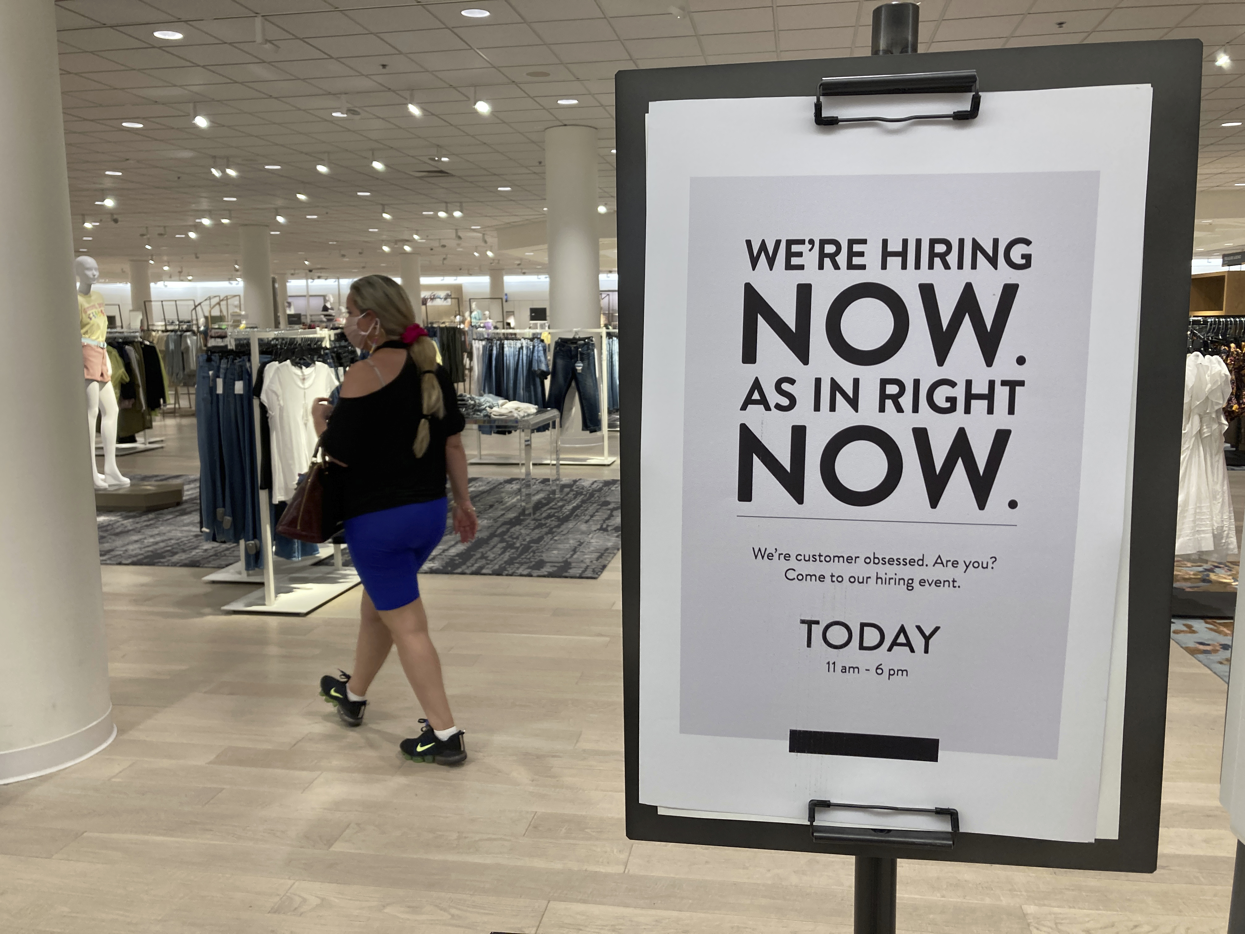 A customer walks behind a sign at a Nordstrom store seeking employees, in Coral Gables, Florida, US