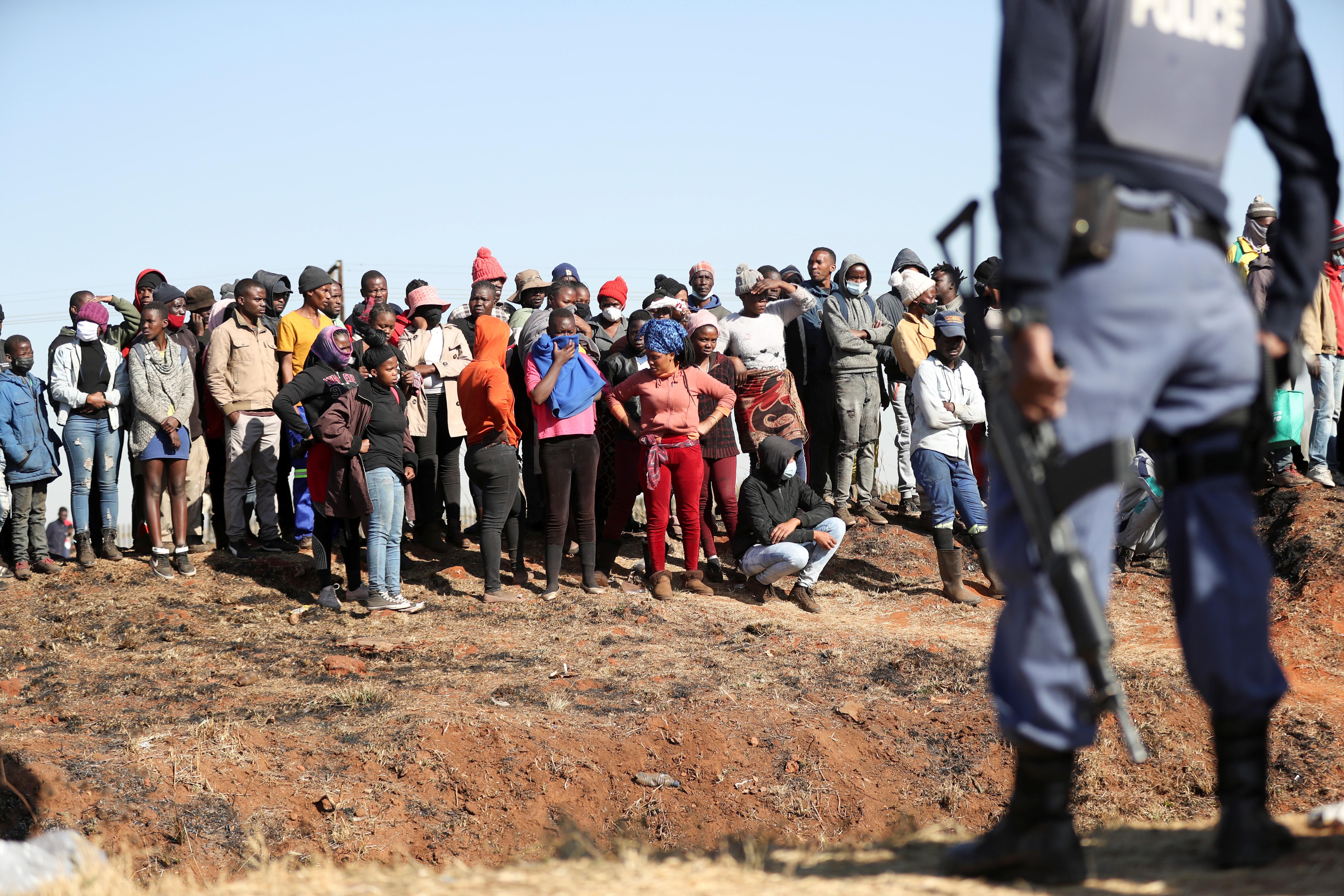 A police officer stands guard in front of protesters as the government deploys the army to quell unrest in Vosloorus, South Africa