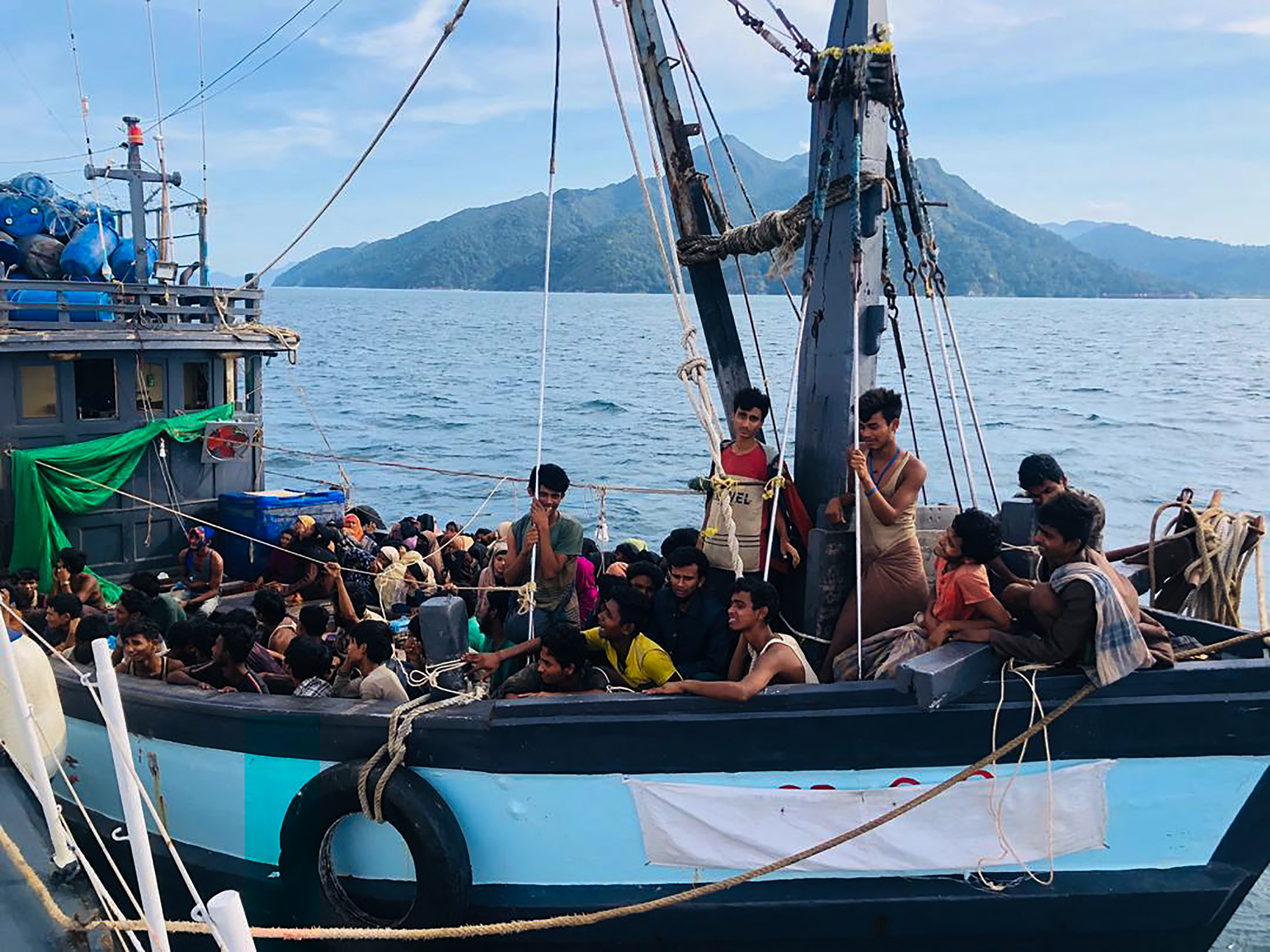 Rphingya packed into a wooden boat off the coast of Langkawi in Malaysia, There is a tyre hanginhulled boat off the side of the blue