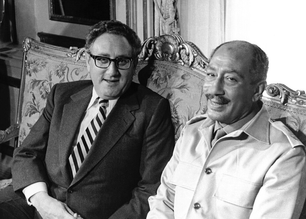 Henry Kissinger and Anwar Sadat seated on a floral couch.