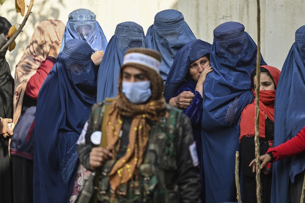 A Taliban fighter stands guard as women wait in a queue during a World Food Programme cash distribution in Kabul on November 29, 2021.