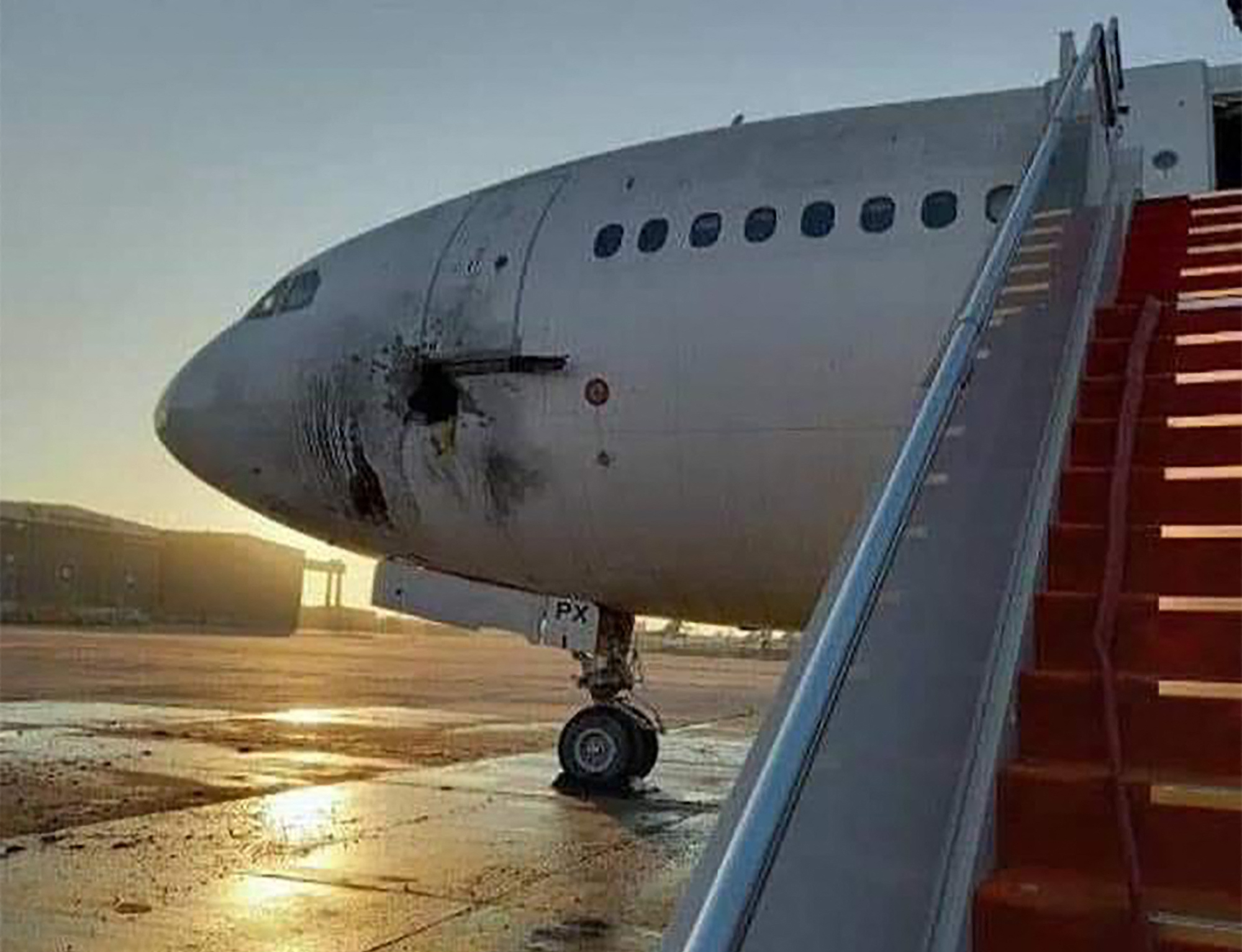a damaged stationary aircraft on the tarmac of Baghdad airport