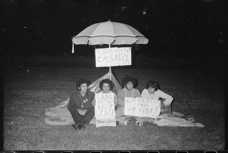 A black and white photo from 1972 showing the Aboriginal Embassy under a beach umbrella. Left to right: Michael Anderson, Billy Craigie, Bert Williams and Tony Coorey.