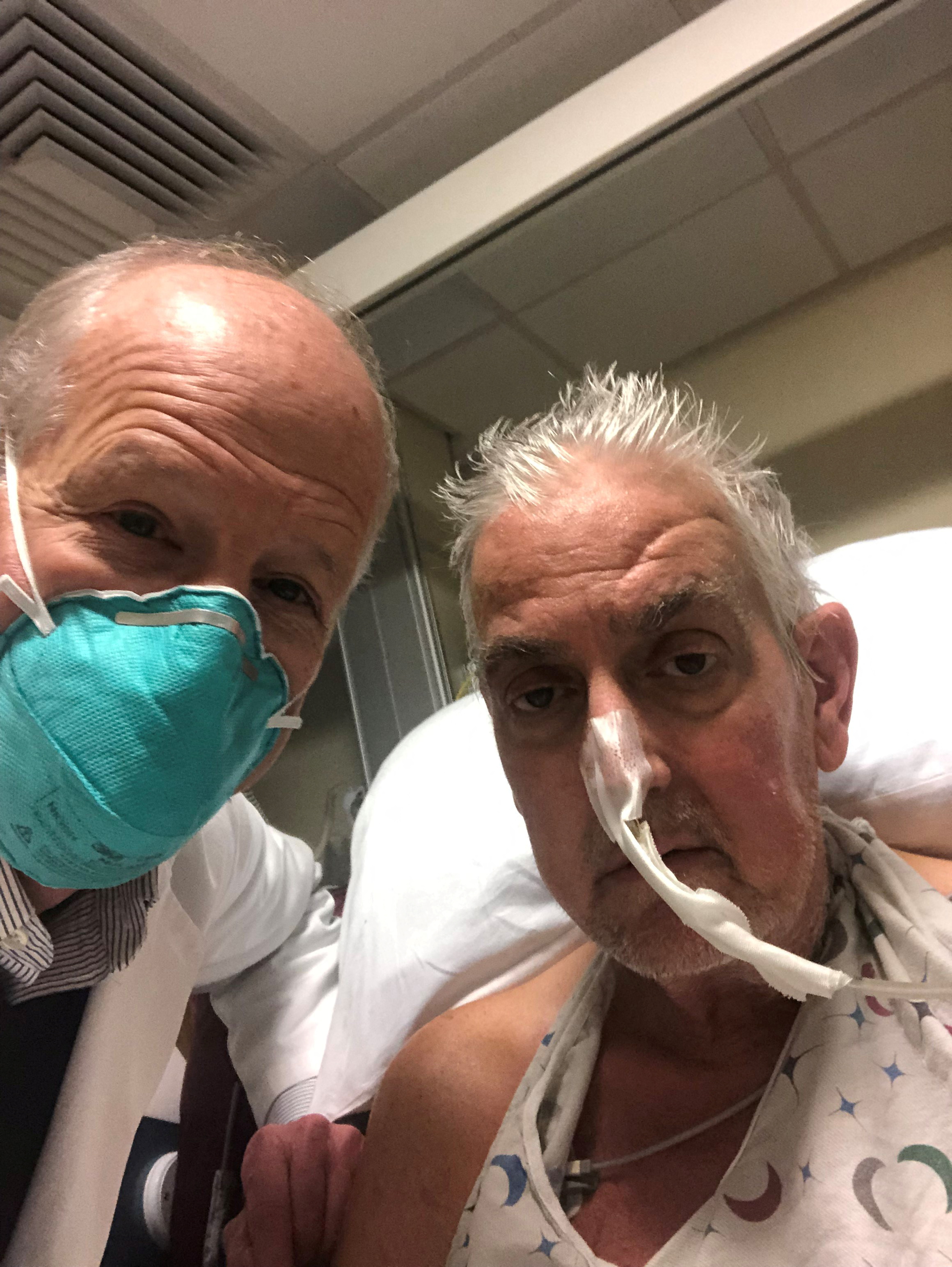 David Bennett, a 57-year-old patient with terminal heart disease, poses with his surgeon. Bennett is sitting up in his hospital bed and has a tube attached to his nose 