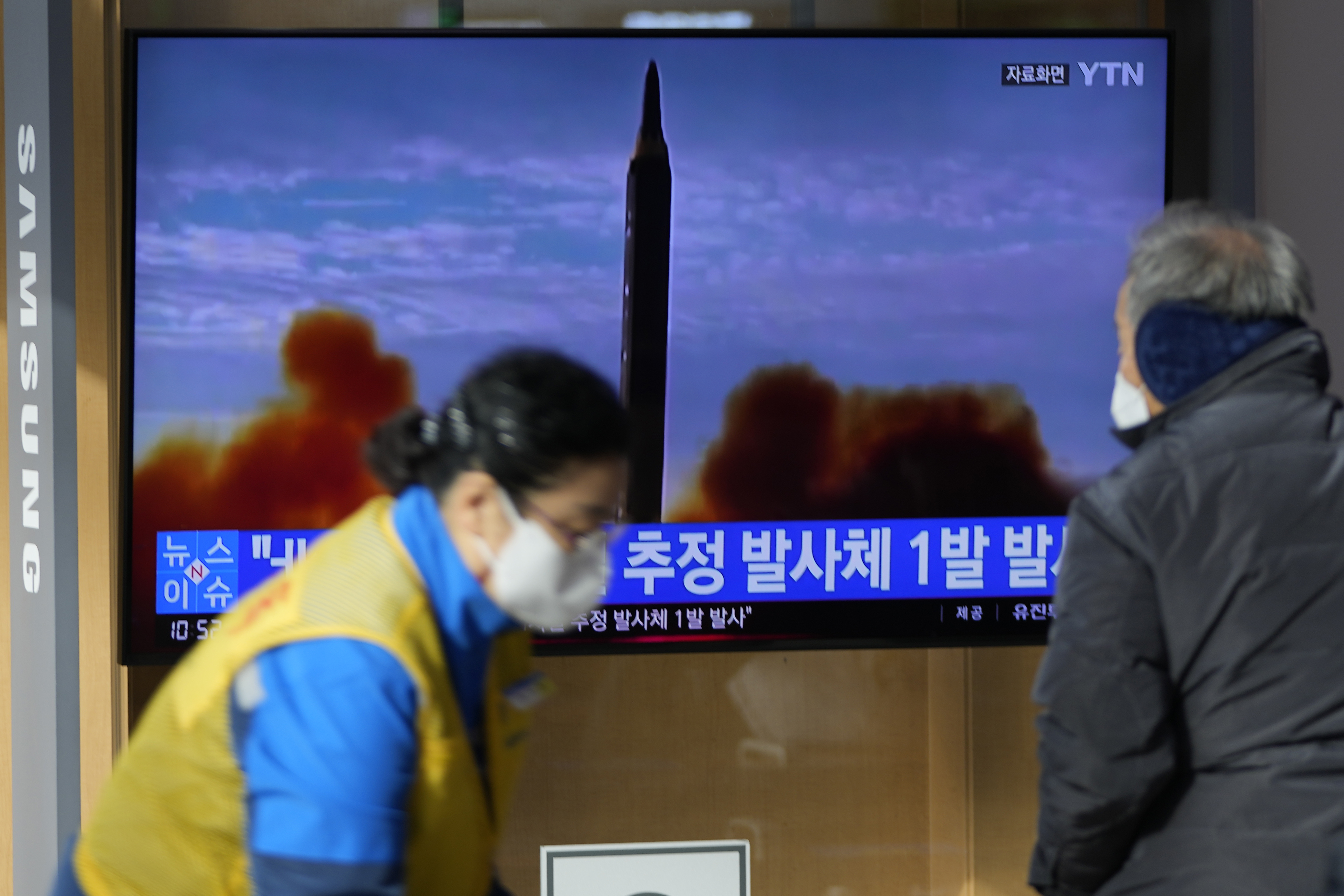 People in masks in front of a television screen showing a news update on North Korea's latest suspected missile launch