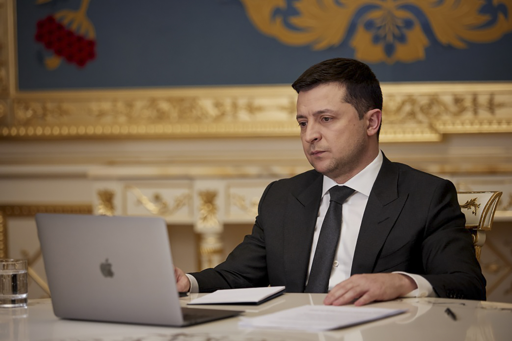 Ukrainian President Volodymyr Zelenskyy sits at a table in front of a laptop and answers during his on-line interview for media in Kyiv, Ukraine