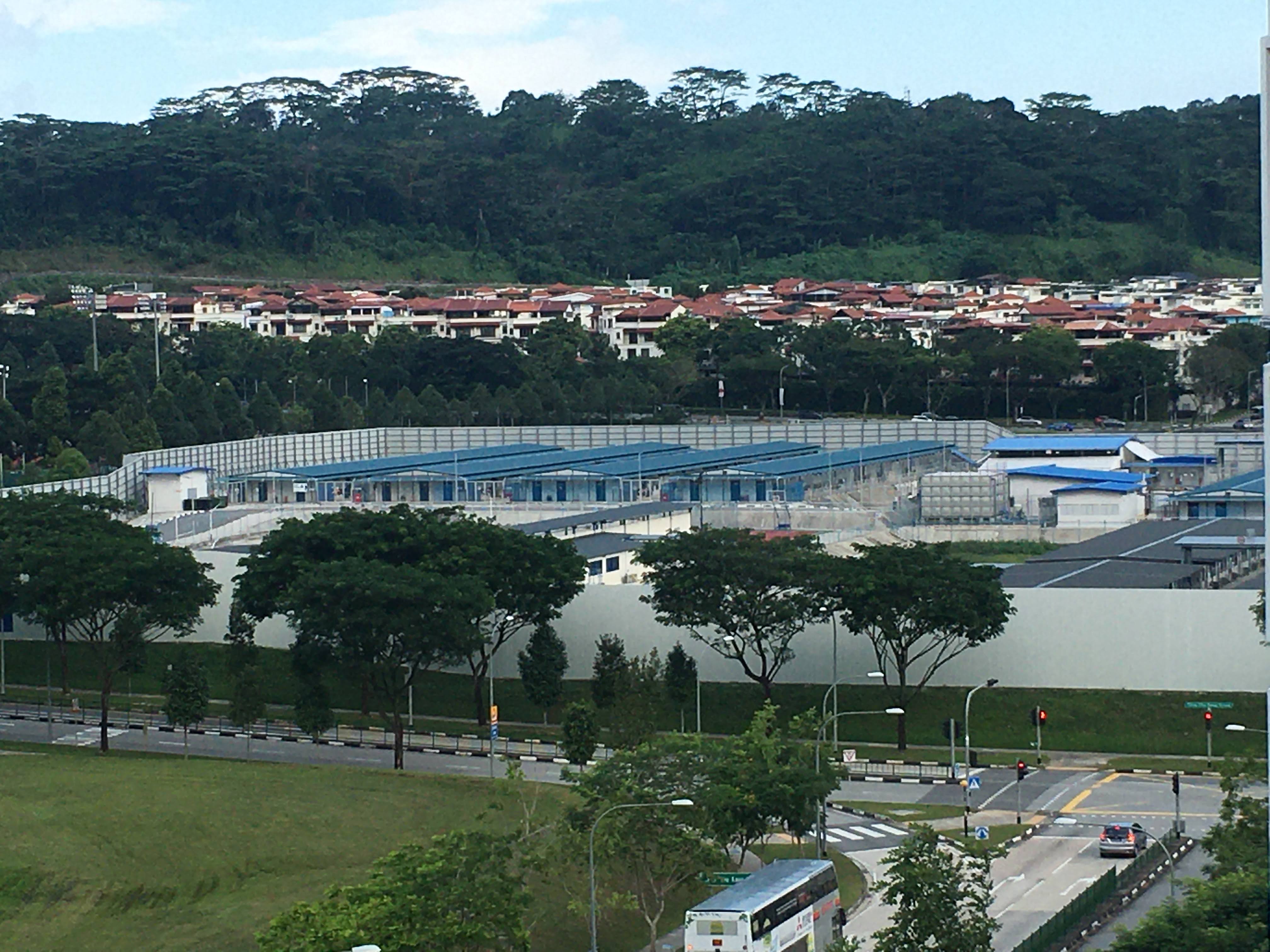 The dormitory compound for migrant workers with its blue roofs, perimeter grey wall and barbed wire 