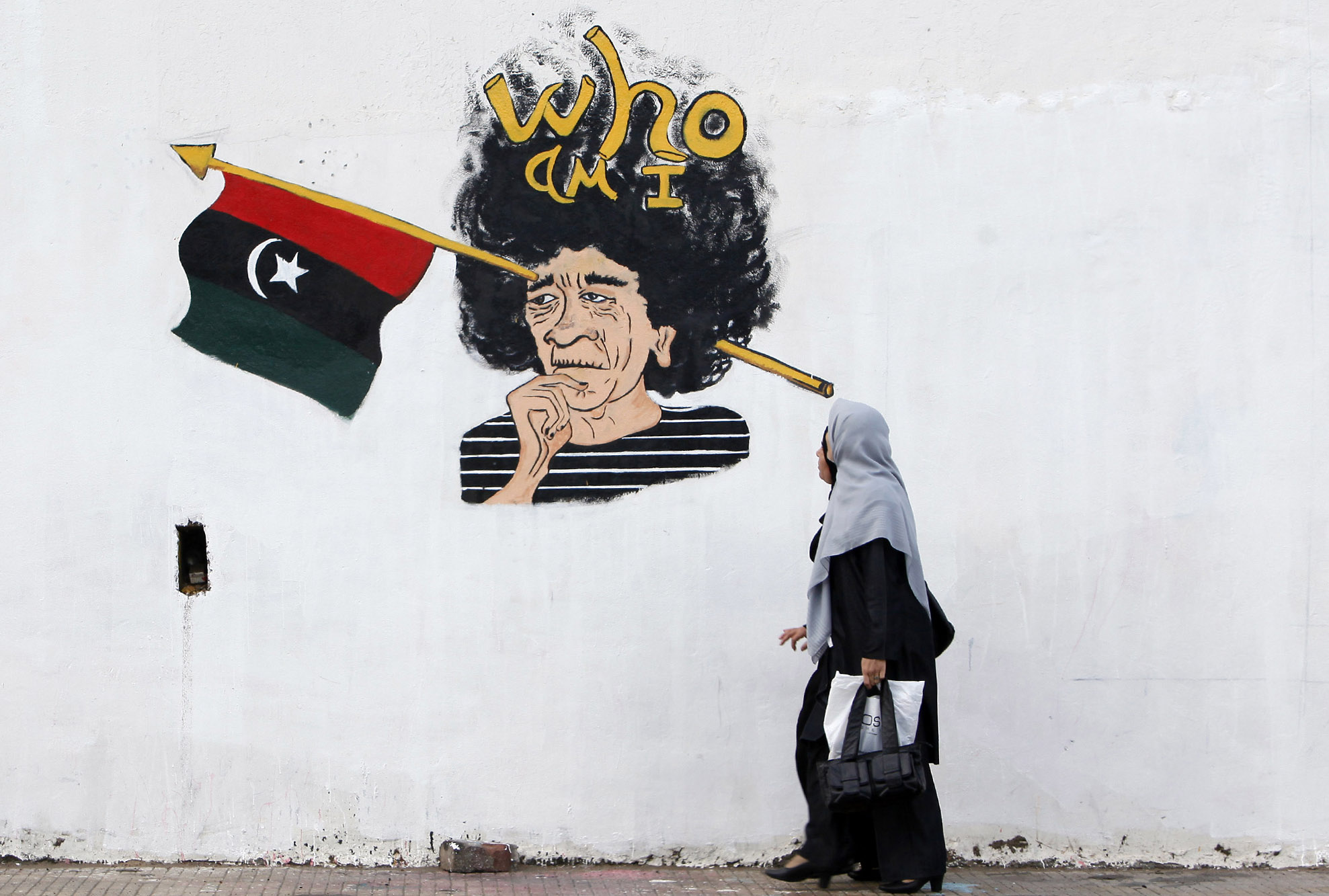 Two Libyan women walk past graffiti depicting Muammar Gaddafi