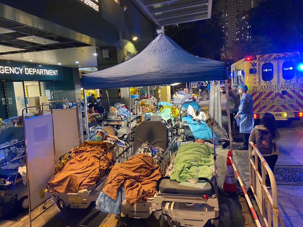 Patients, many of them elderly, cover themselves with blankets as they wait outside in the cold for admission to hospital