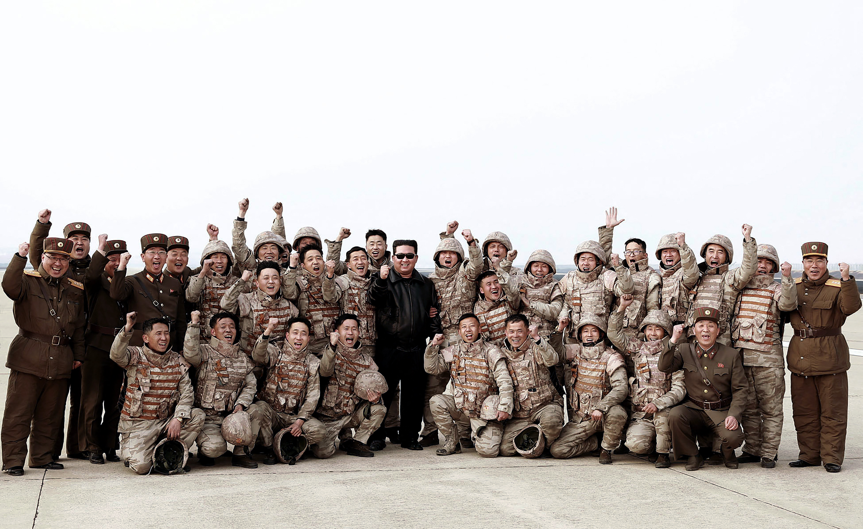 Kim Jong Un, dressed in black leather bomber jacket and dark glasses, poses with member of the armed forces