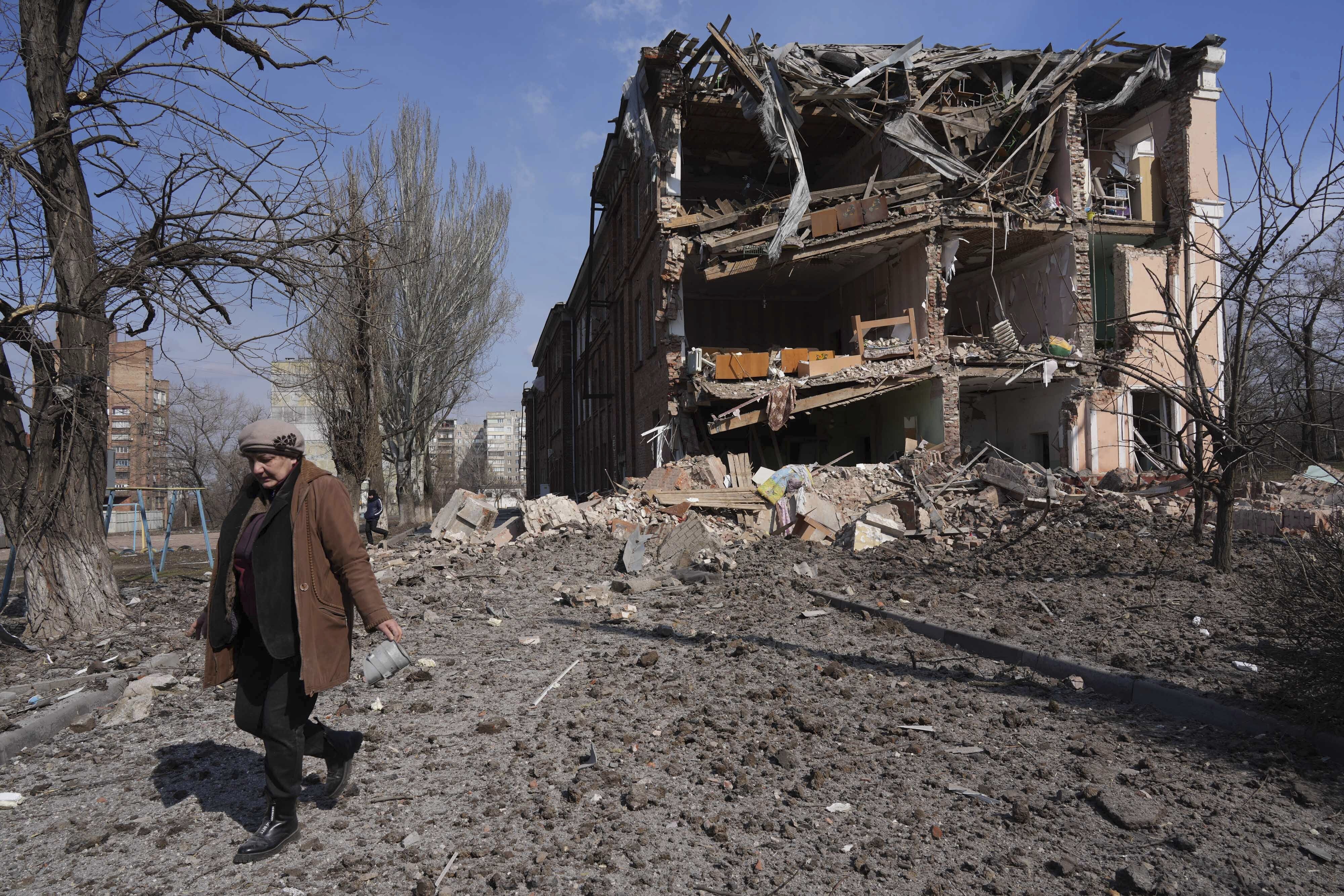 A woman walks past building damaged by shelling in Mariupol, Ukraine