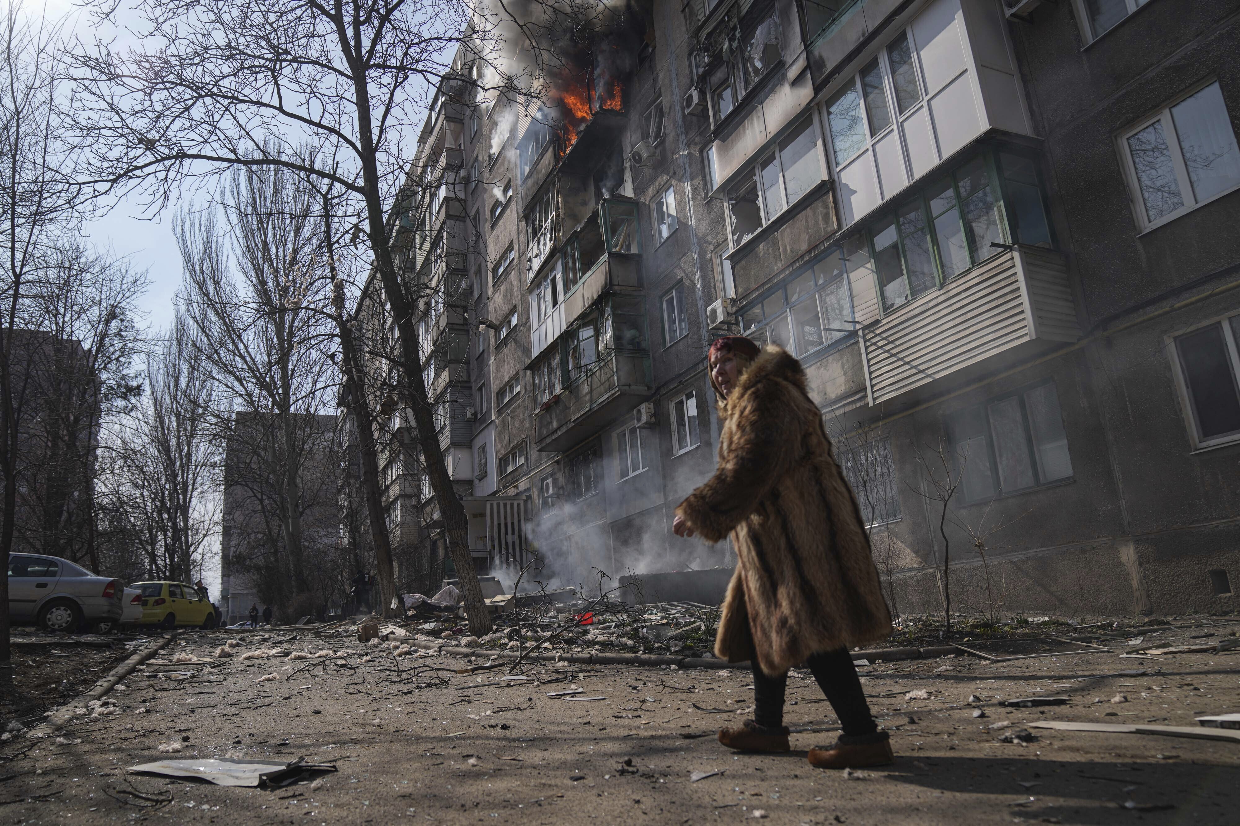 A woman walks past a burning apartment building after shelling in Mariupol