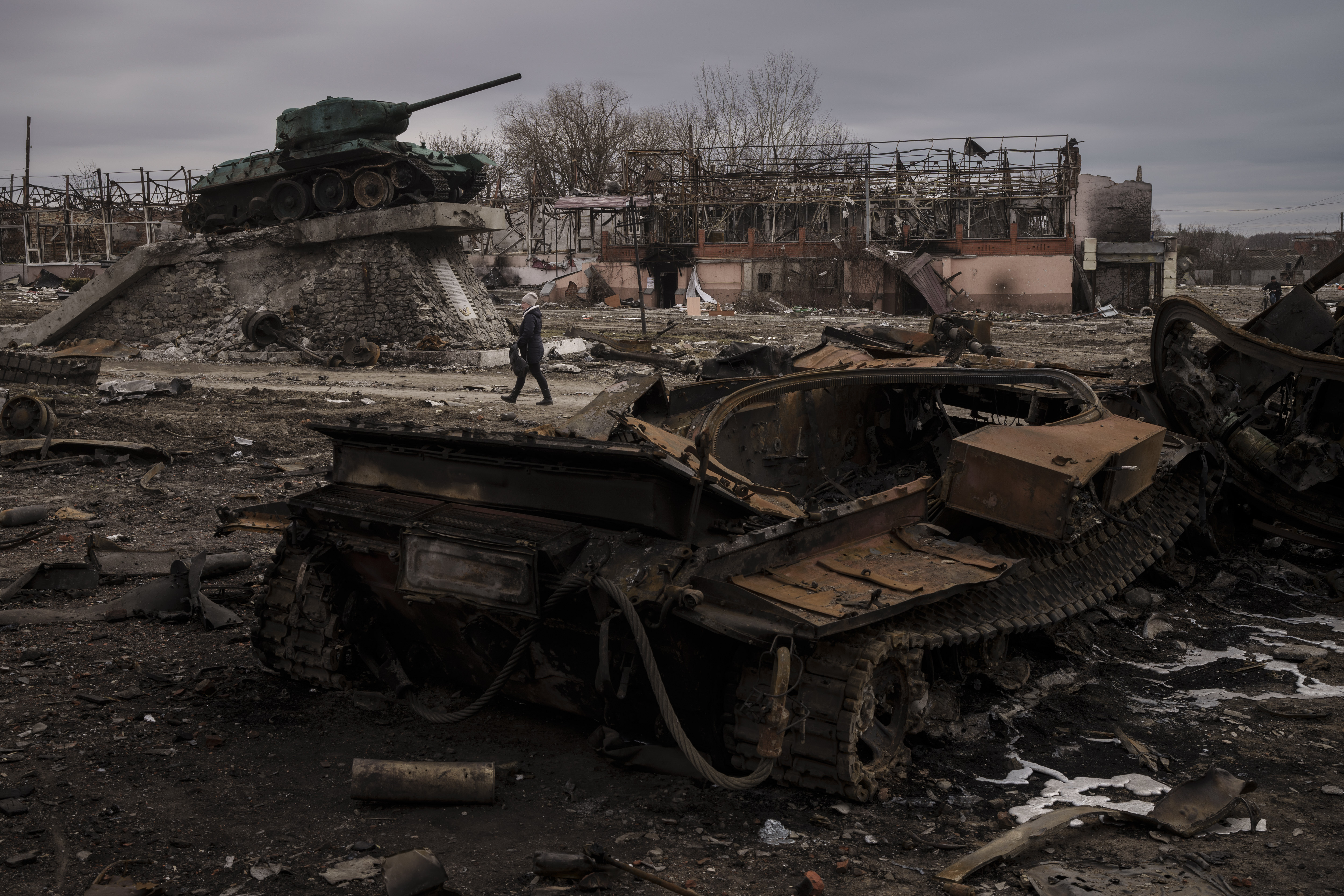 A woman walks past a destroyed tank in the town of Trostsyanets, Ukraine