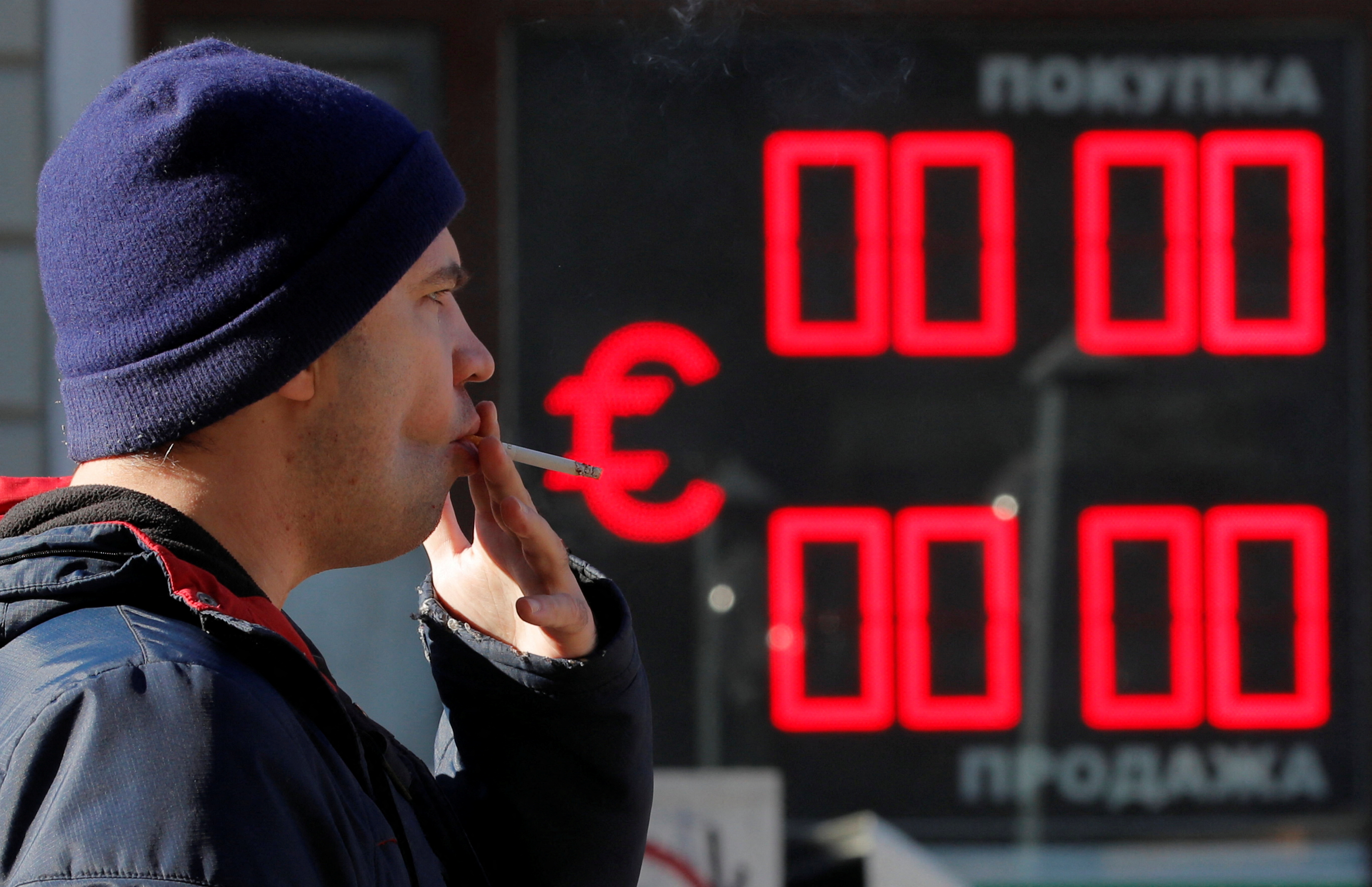 A man smokes as he walks past a currency exchange office in Saint Petersburg, Russia