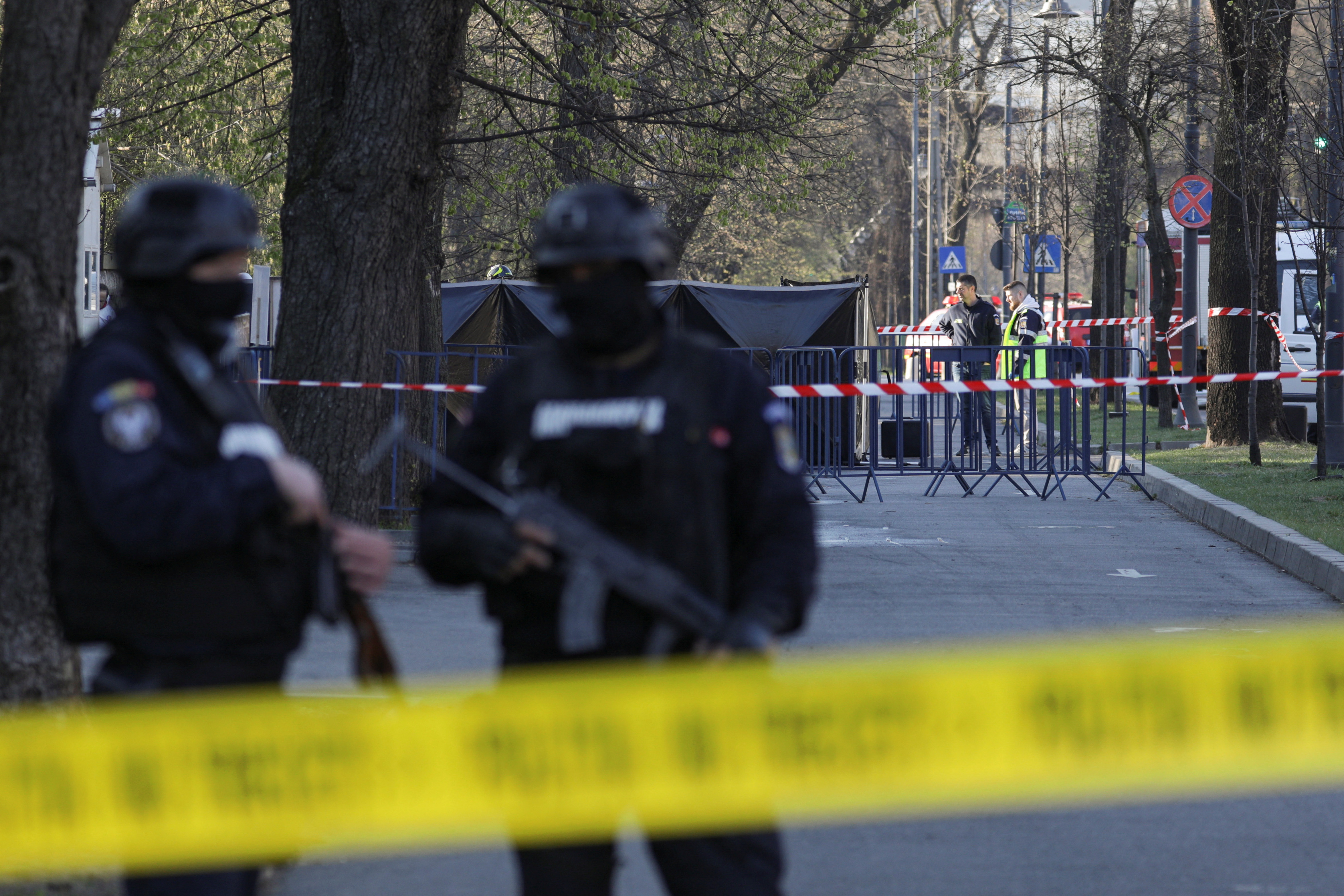 Police officers stand guard as crime scene investigators check the area where a car crashed into the gate of the Russian Embassy in Bucharest