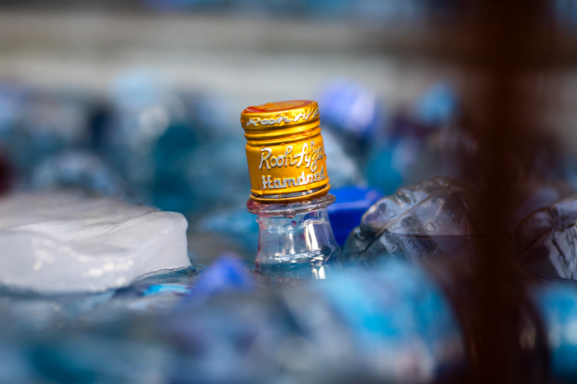 The cap of a Rooh Afza bottle that's been refilled with the prepared drink is seen among chilling bottles of water and chunks of ice