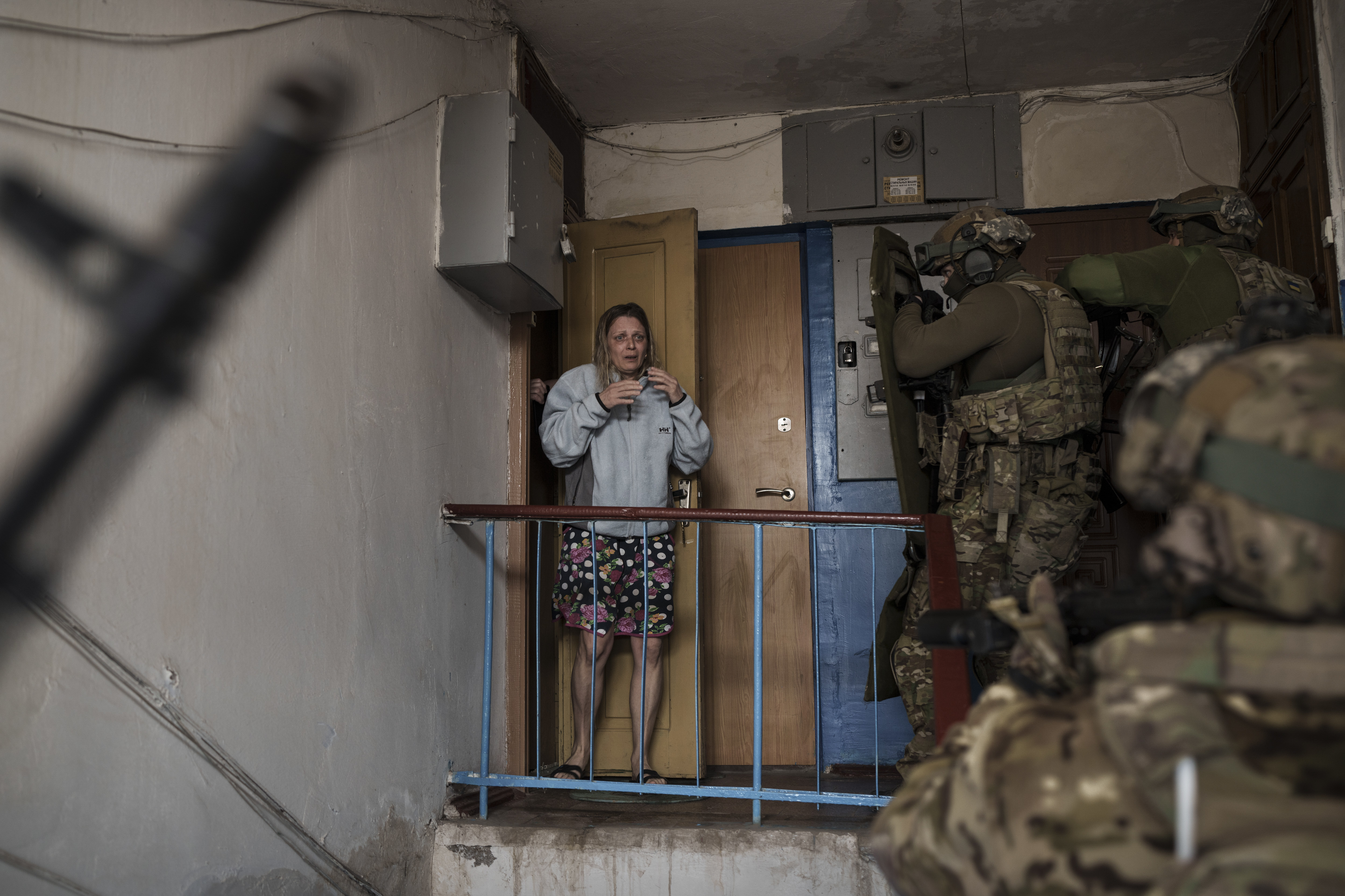 An alarmed looking woman looks as Security Service of Ukraine (SBU) service members come up the stairs of her building during an operation to arrest suspected Russian collaborators in Kharkiv.