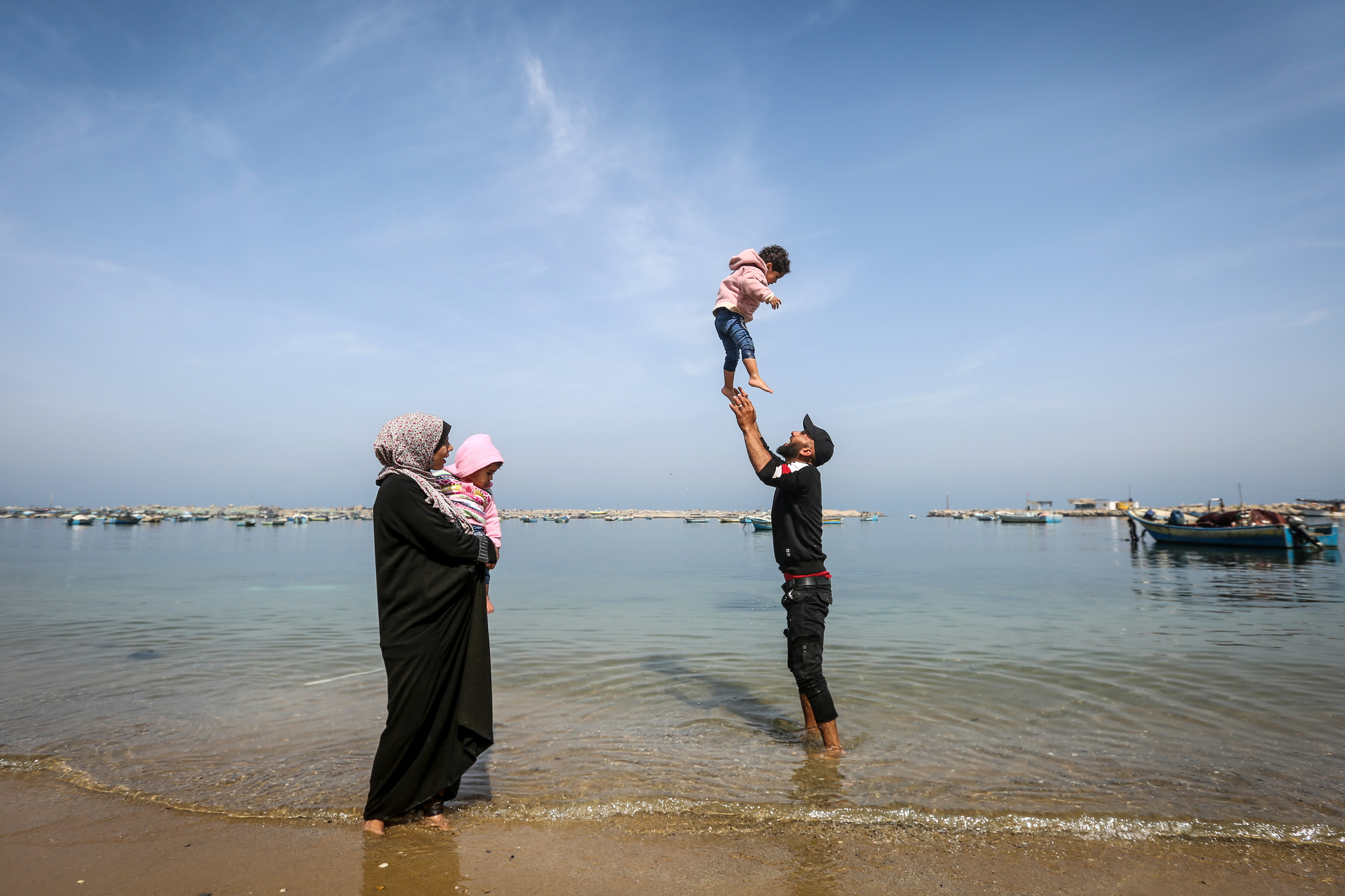 At the water's edge, Khadr plays with Sandy as Madelyn stands by holding Safinaz
