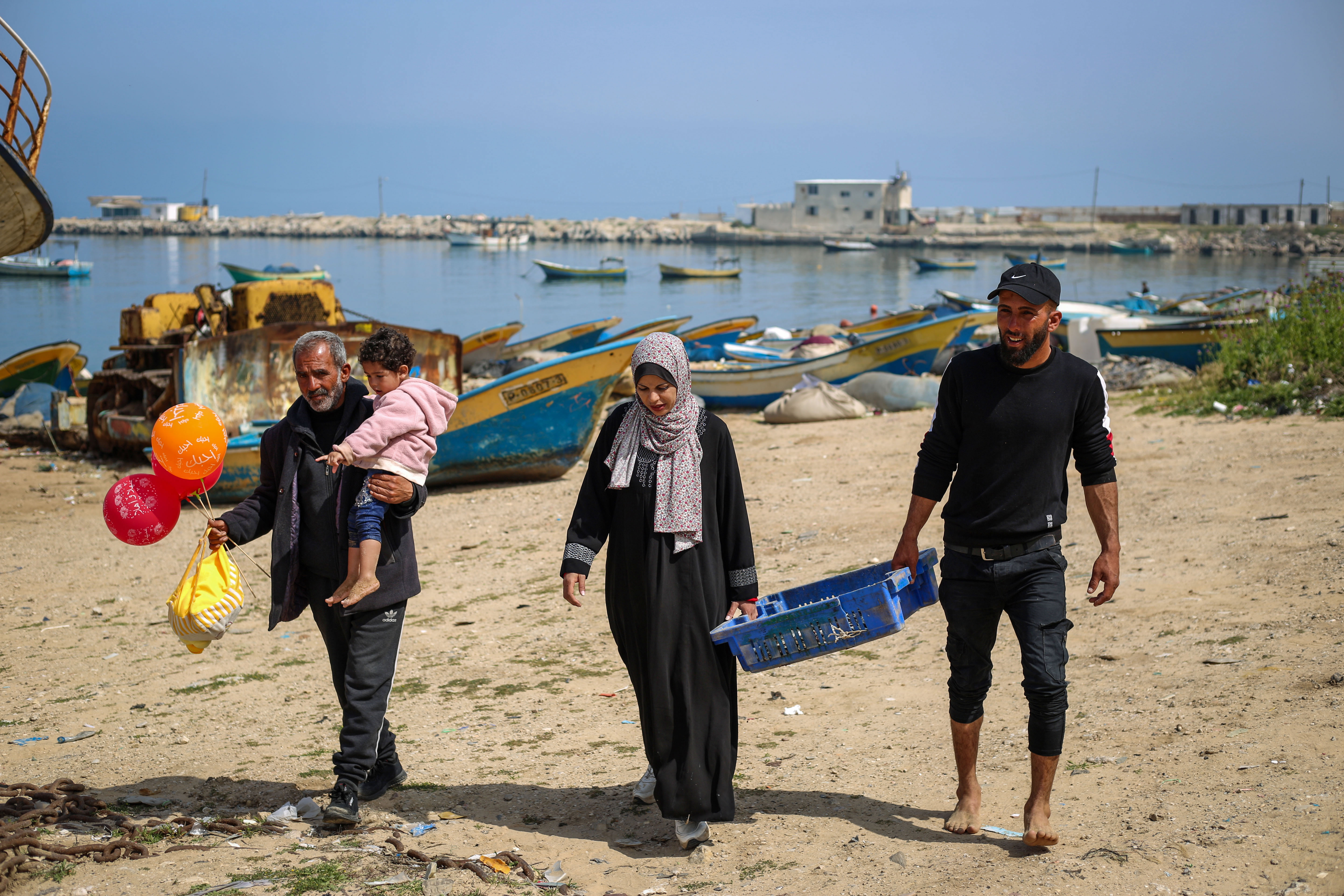 Jamal carries his granddaughter and walks next to Madelyn and Khadr who are carrying the fish