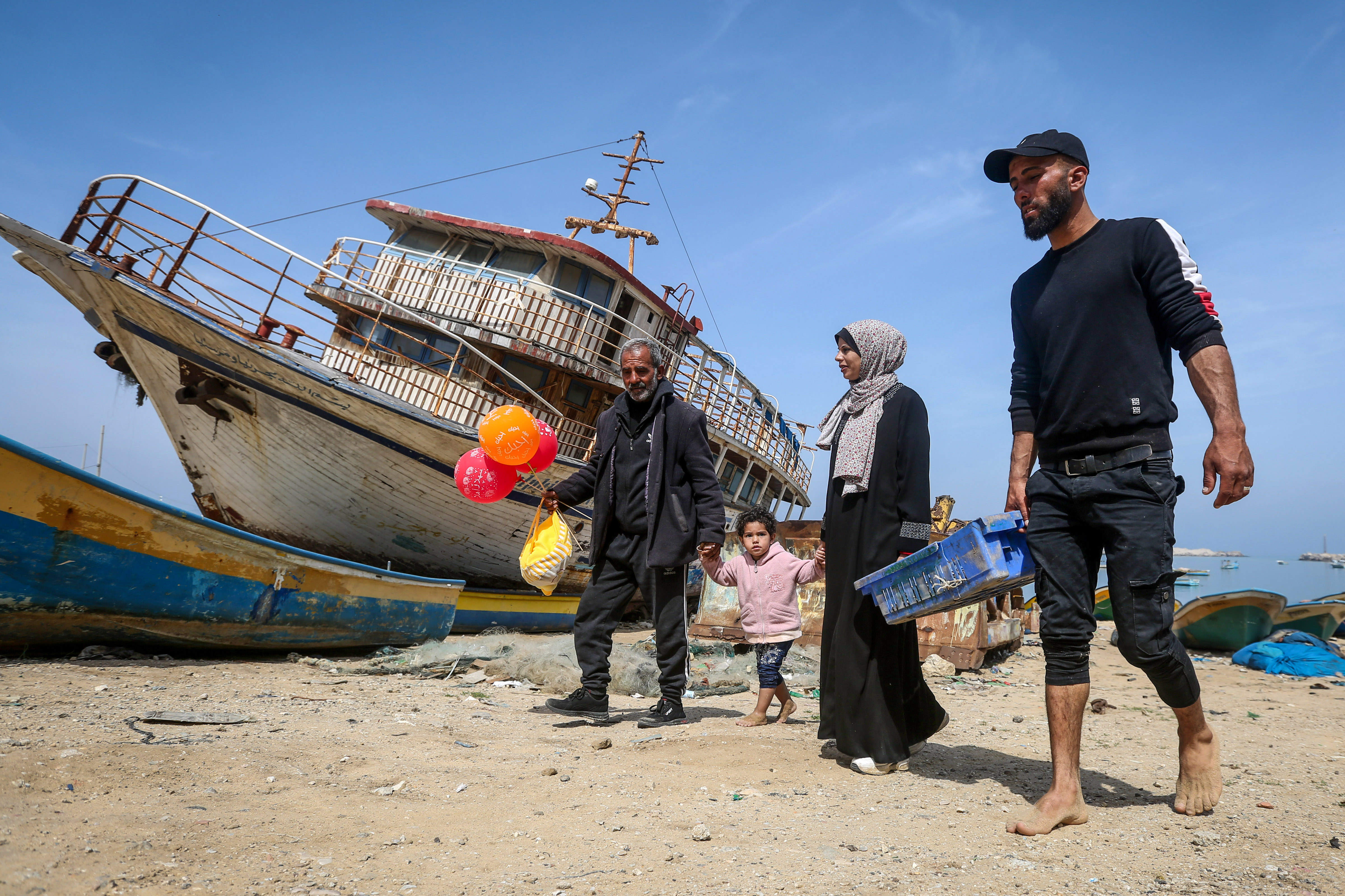Khadr, Madelyn and Jamal walk along with little Sandy with a beached boat behind them on the beach