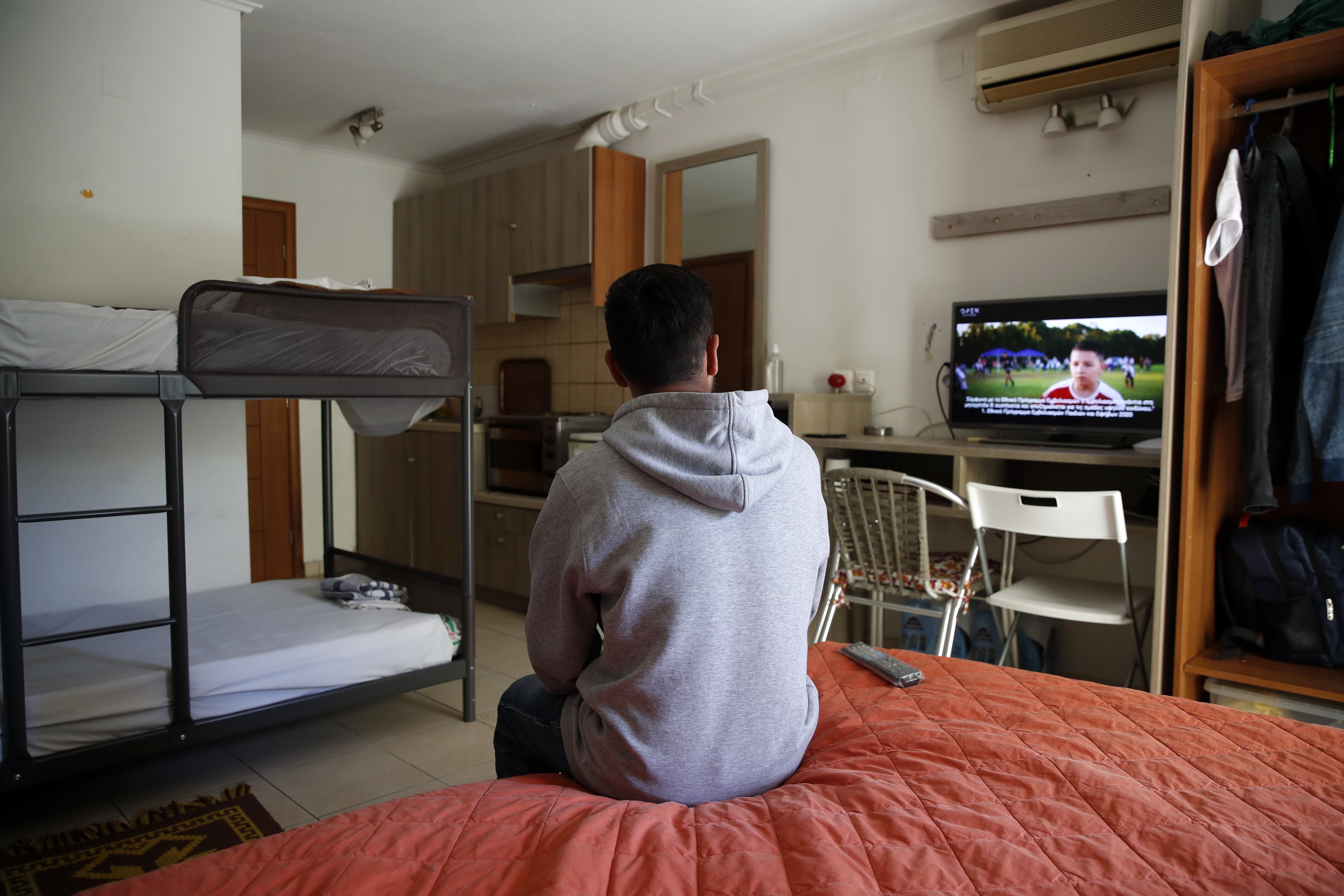 An Afghan father watches television in his room, at the port of Vathy on the eastern Aegean island of Samos, Greece