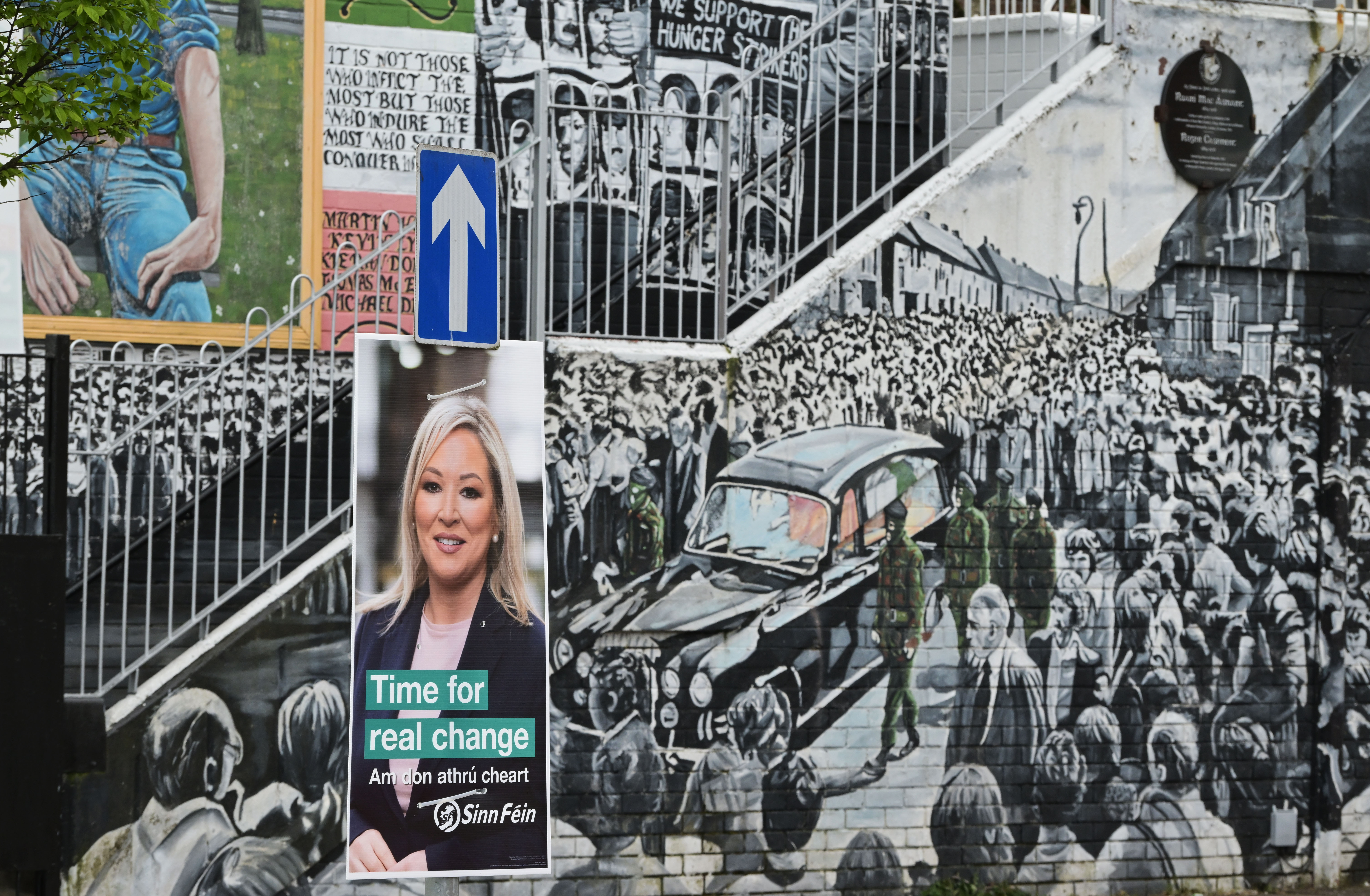 Sinn Féin's Michelle O'Neill election poster is seen against the backdrop of a republican mural in the nationalist area of west Belfast