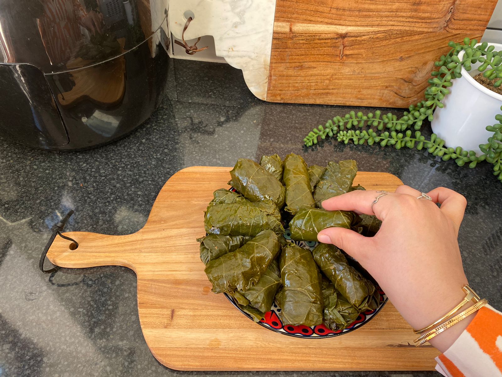 A hand is seen stacking rolled stuffed grape leaves on a plate