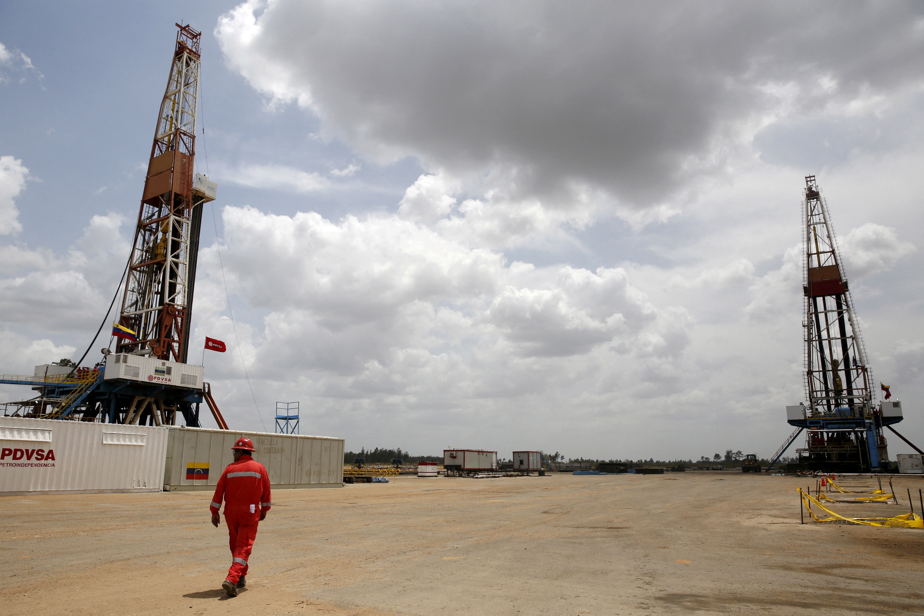 An oilfield worker walks next to drilling rigs at an oil well operated by Venezuela's state oil company PDVSA.