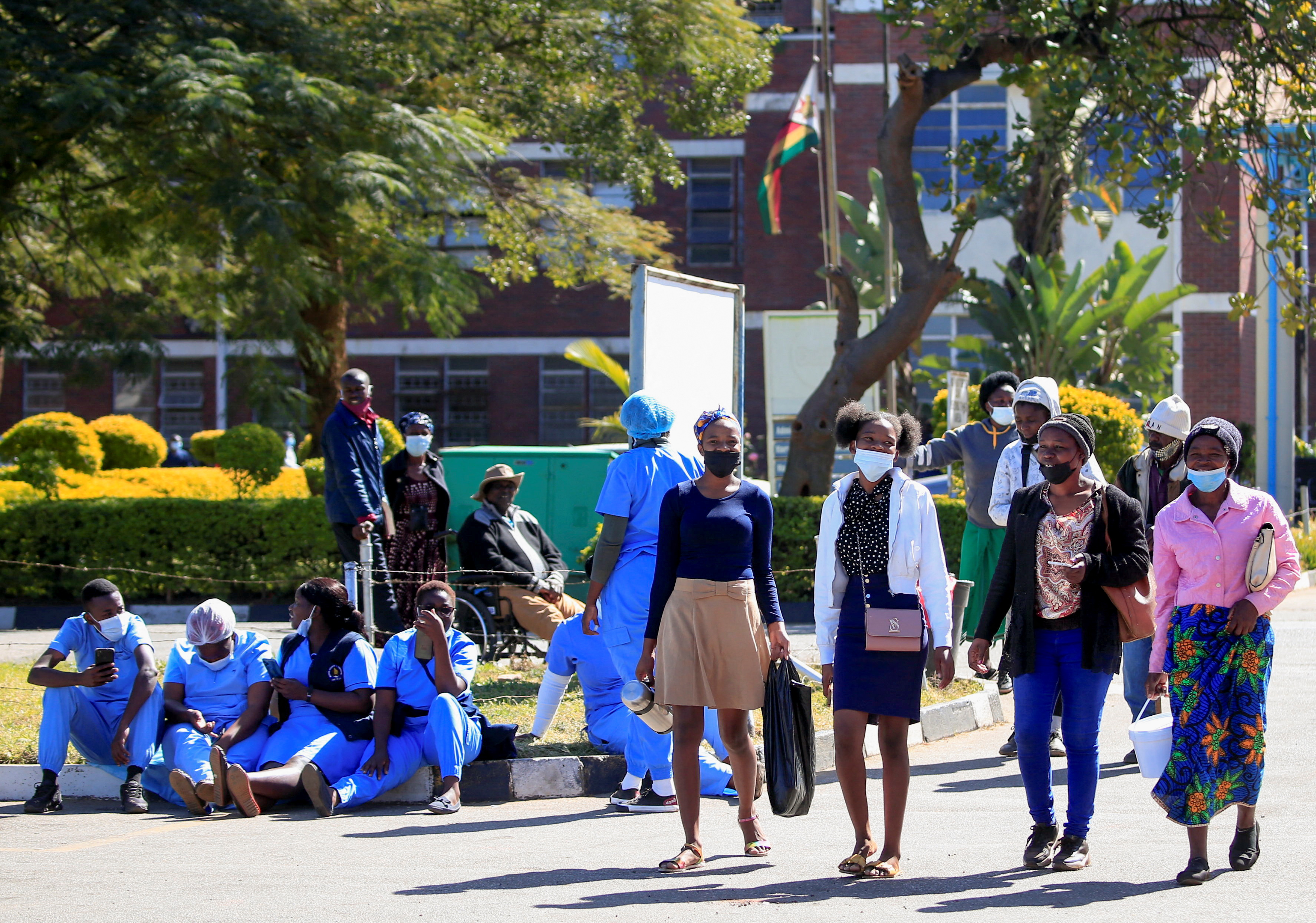 People walk past Zimbabwean medical workers as they sit outside Sally Mugabe Central Hospital during a strike by state doctors and nurses