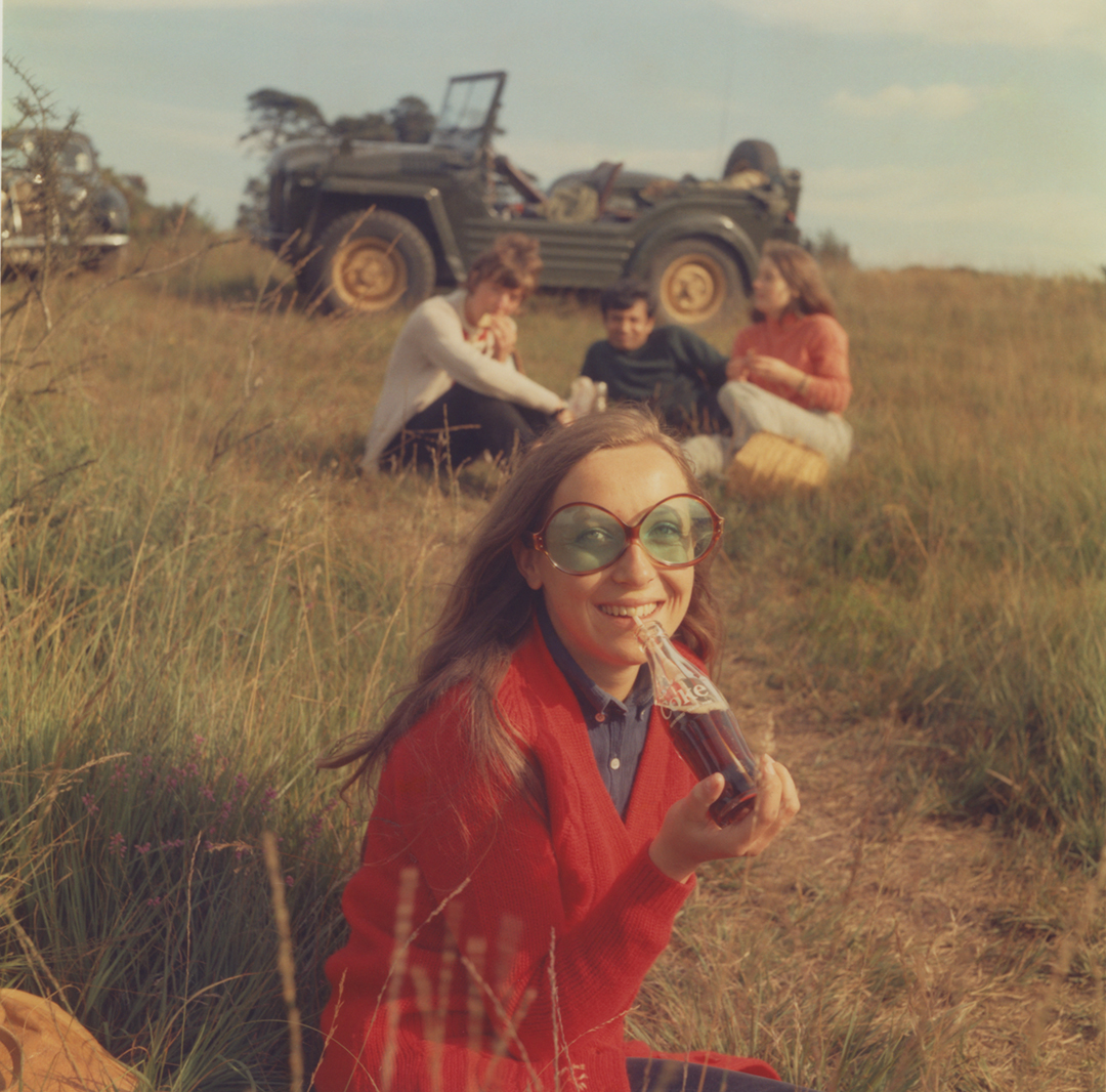 A photo of people sitting in grass eating and drinking.