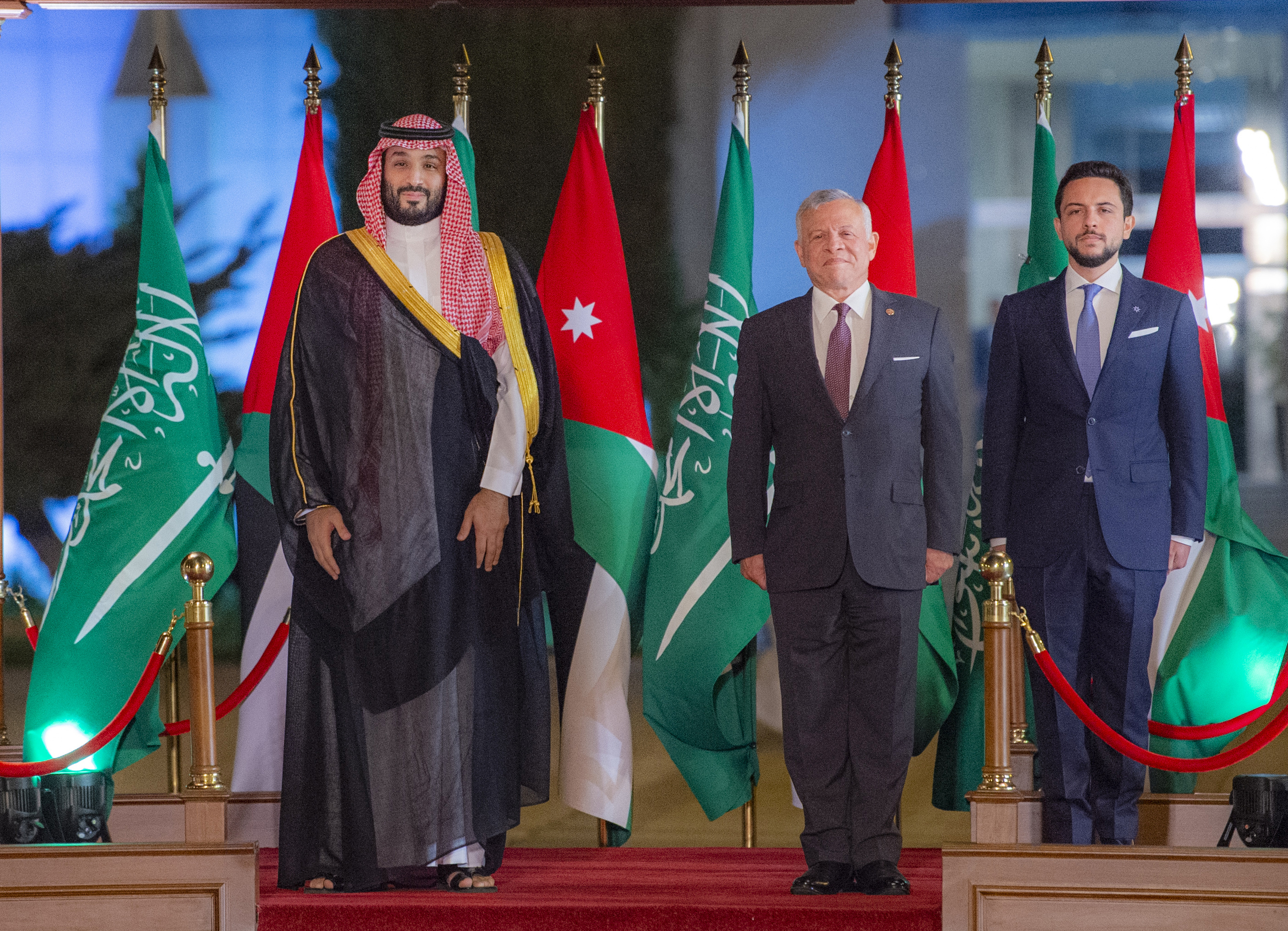 Saudi Crown Prince Mohammed bin Salman, King Abdullah II of Jordan and his son, Crown Prince Hussein bin Abdullah stand together for a photo in front of Saudi and Jordanian flags.