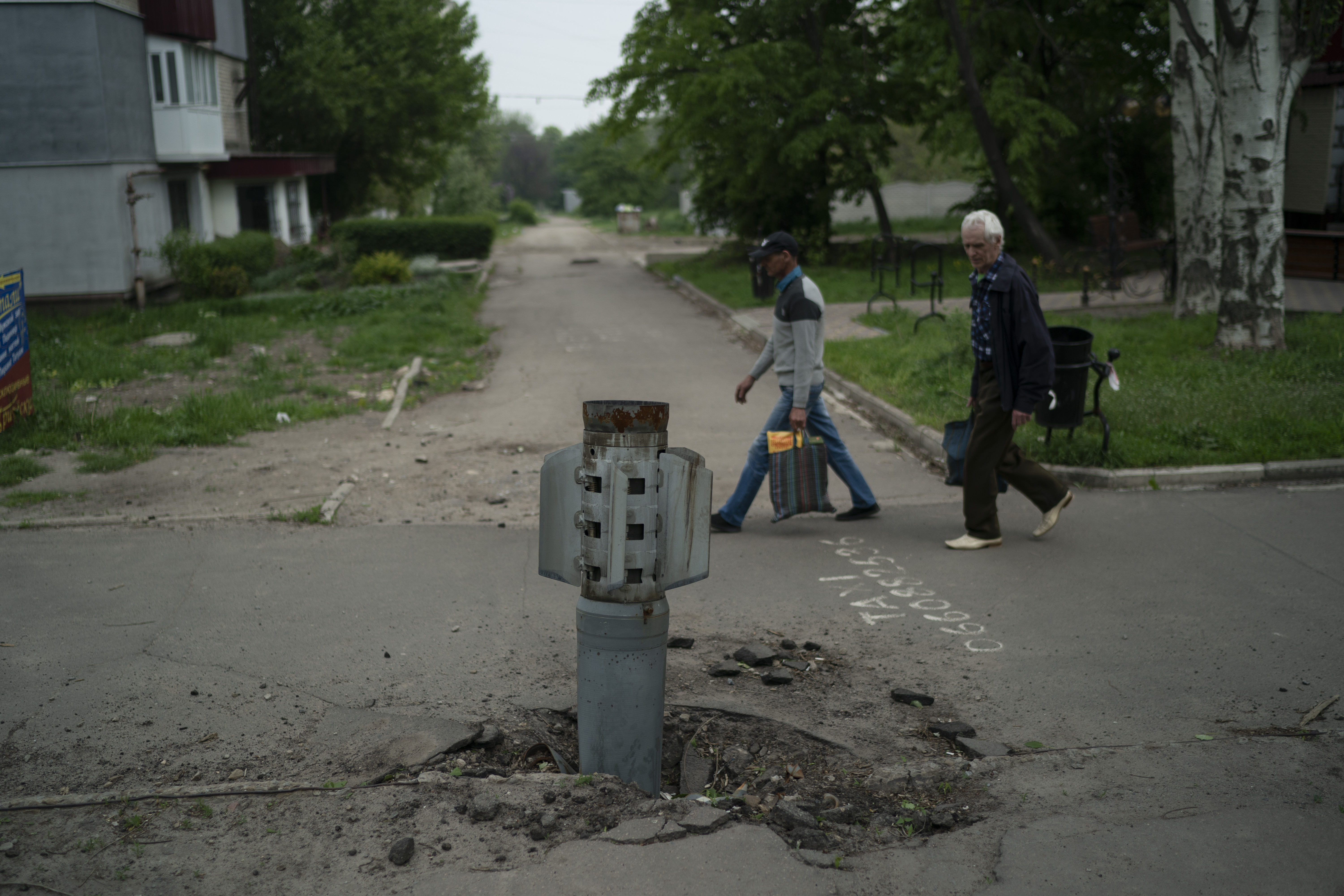 People walk past part of a rocket that sits wedged in the ground