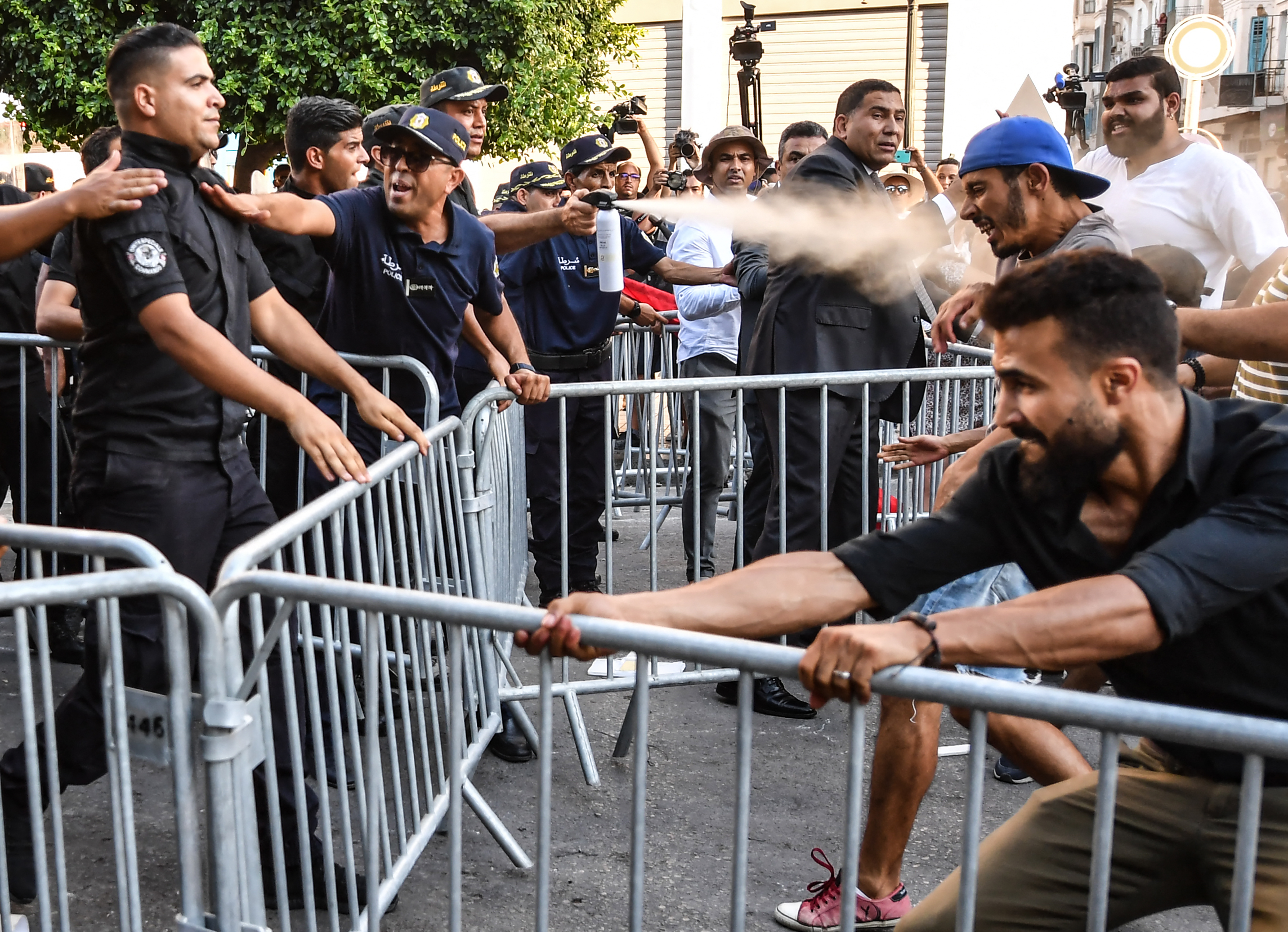 Protesters and police jostle at barriers erected in Tunis with an officer spraying tear gas into their faces