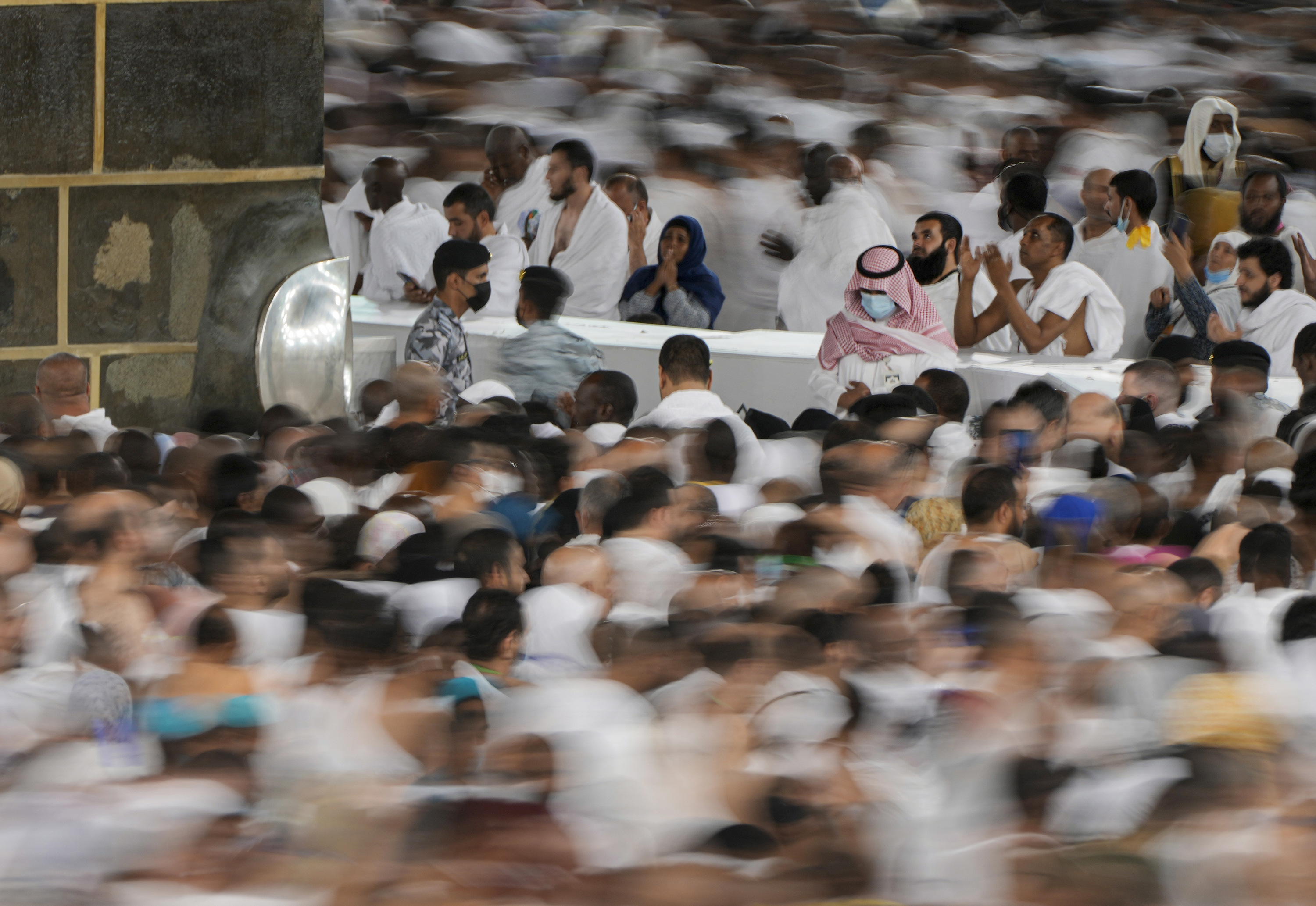 low shutter speed, Muslim pilgrims pray as others circumambulate around the Kaaba