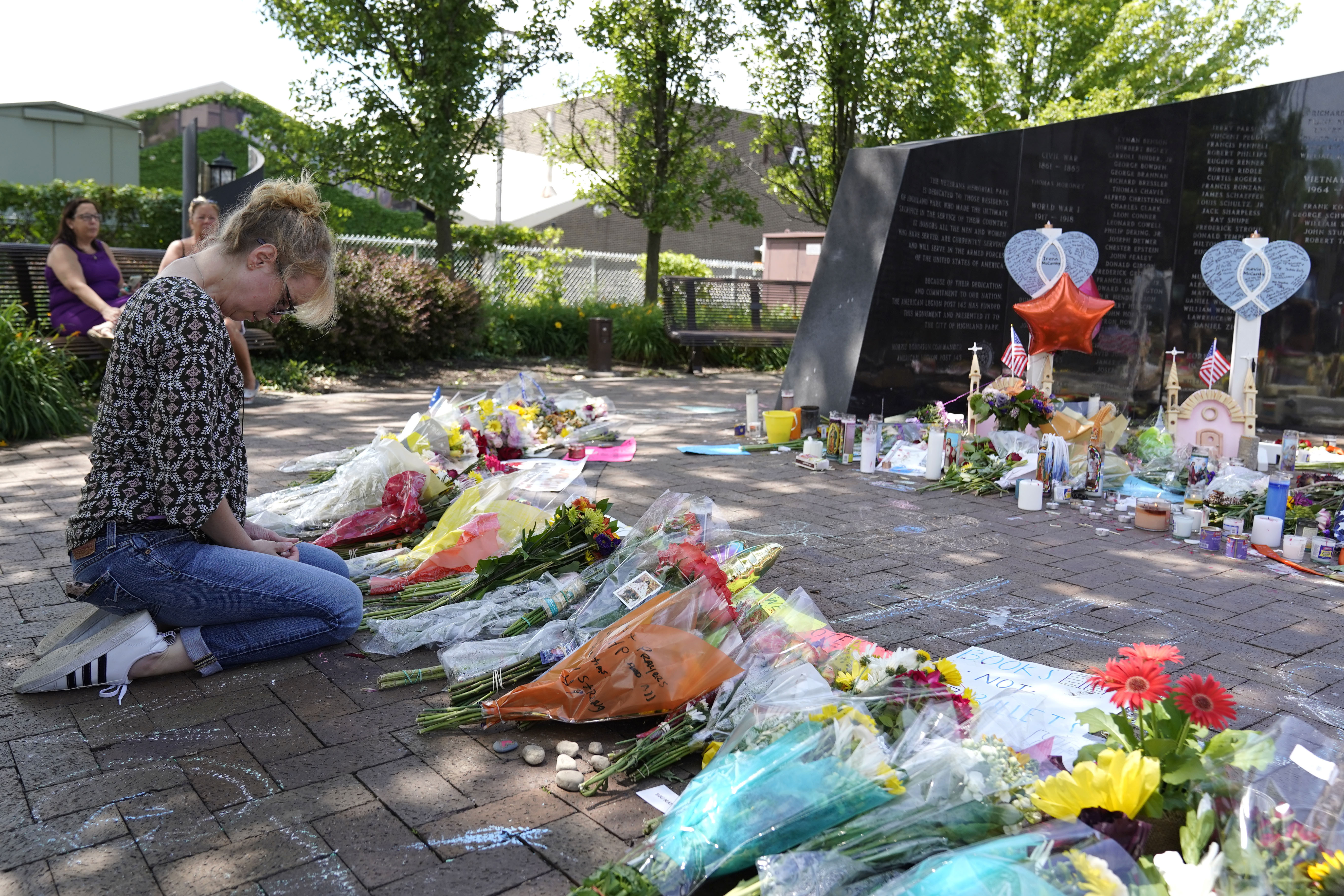 A woman kneels with head bowed in front of a makeshift memorial for victims of the July 4 attack.