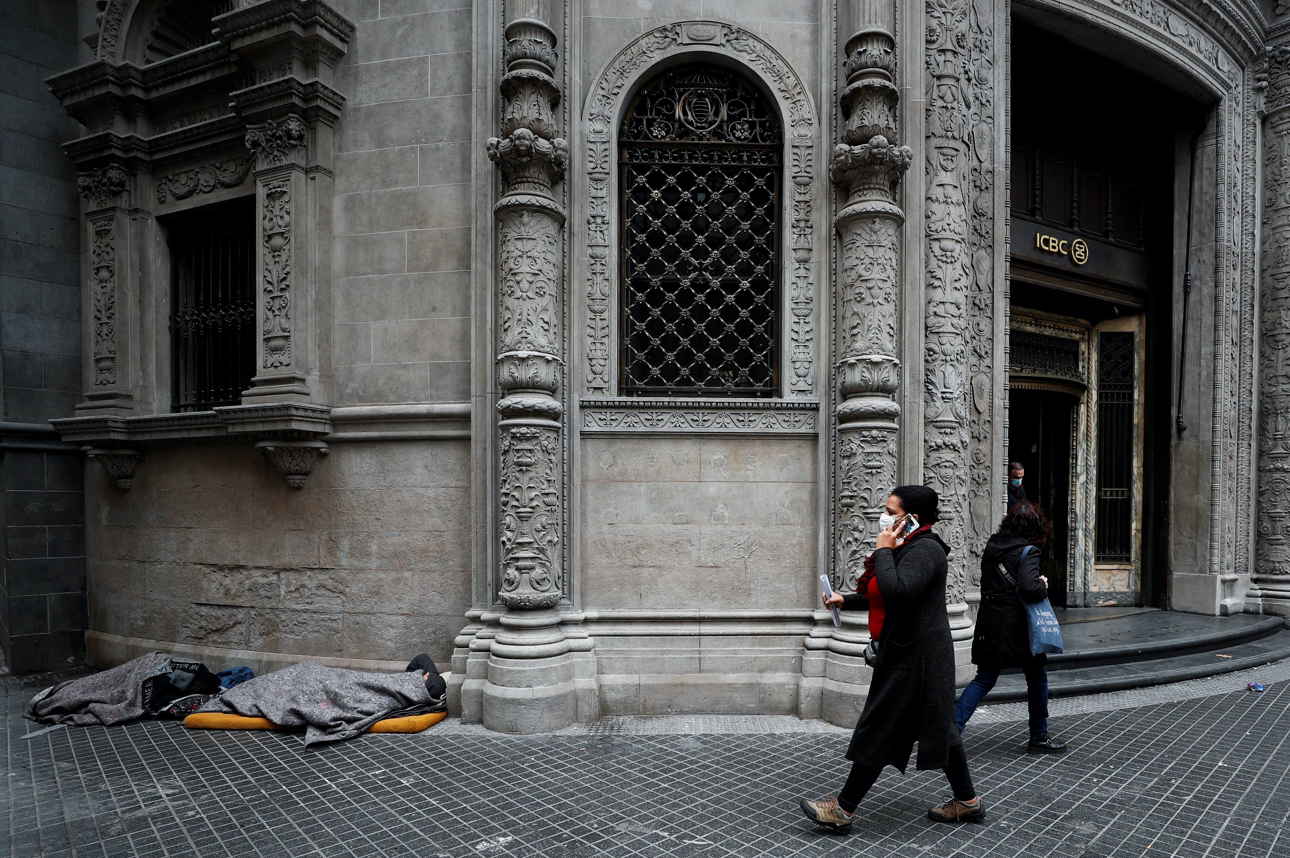 Pedestrians walk past people sleeping outside a bank, in Buenos Aires’ financial district, Argentina