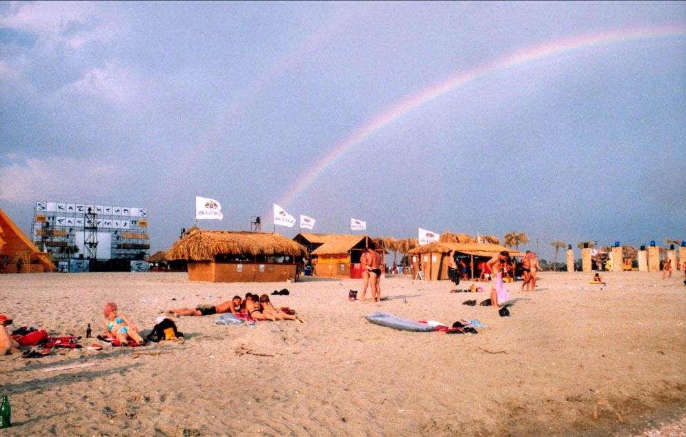 A photo of a beach with people sunbathing and walking around with huts in the background during the KaZantip festival.