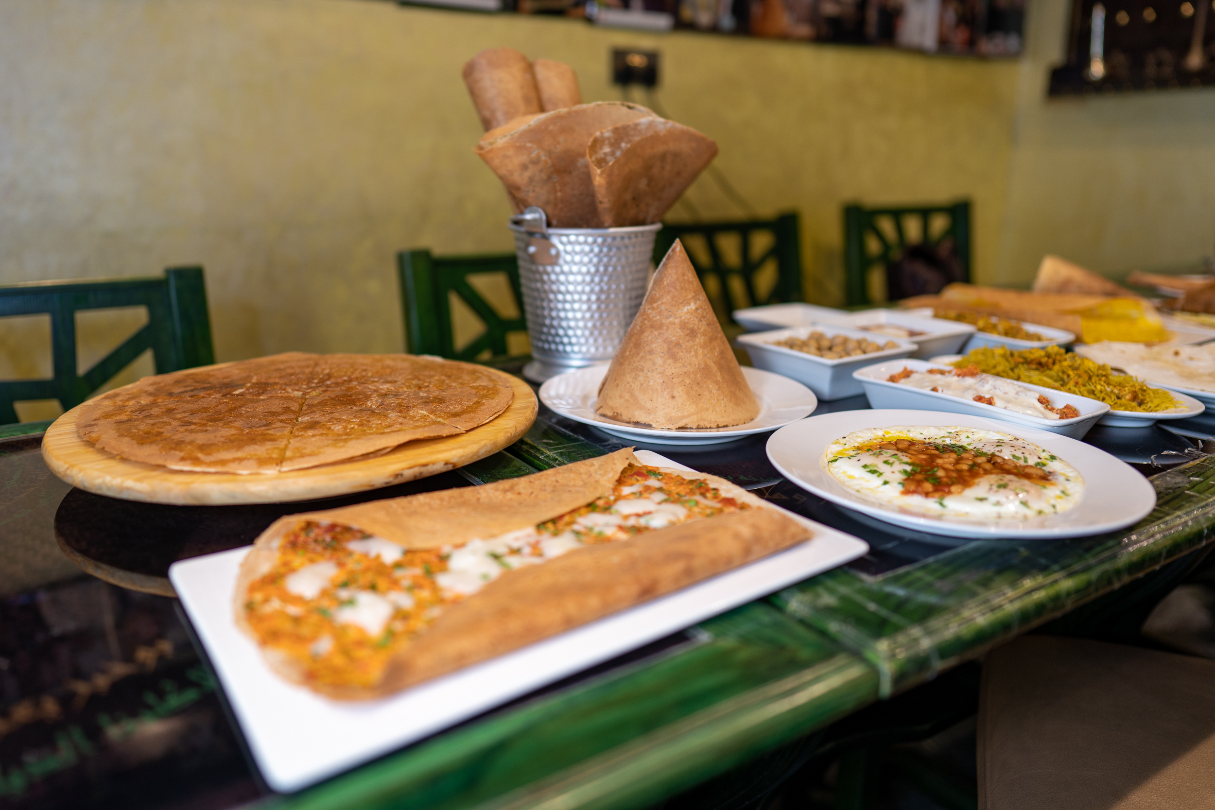 Photo of a green table full of breakfast dishes, regag breads with fillings and without, folded into fanciful shapes