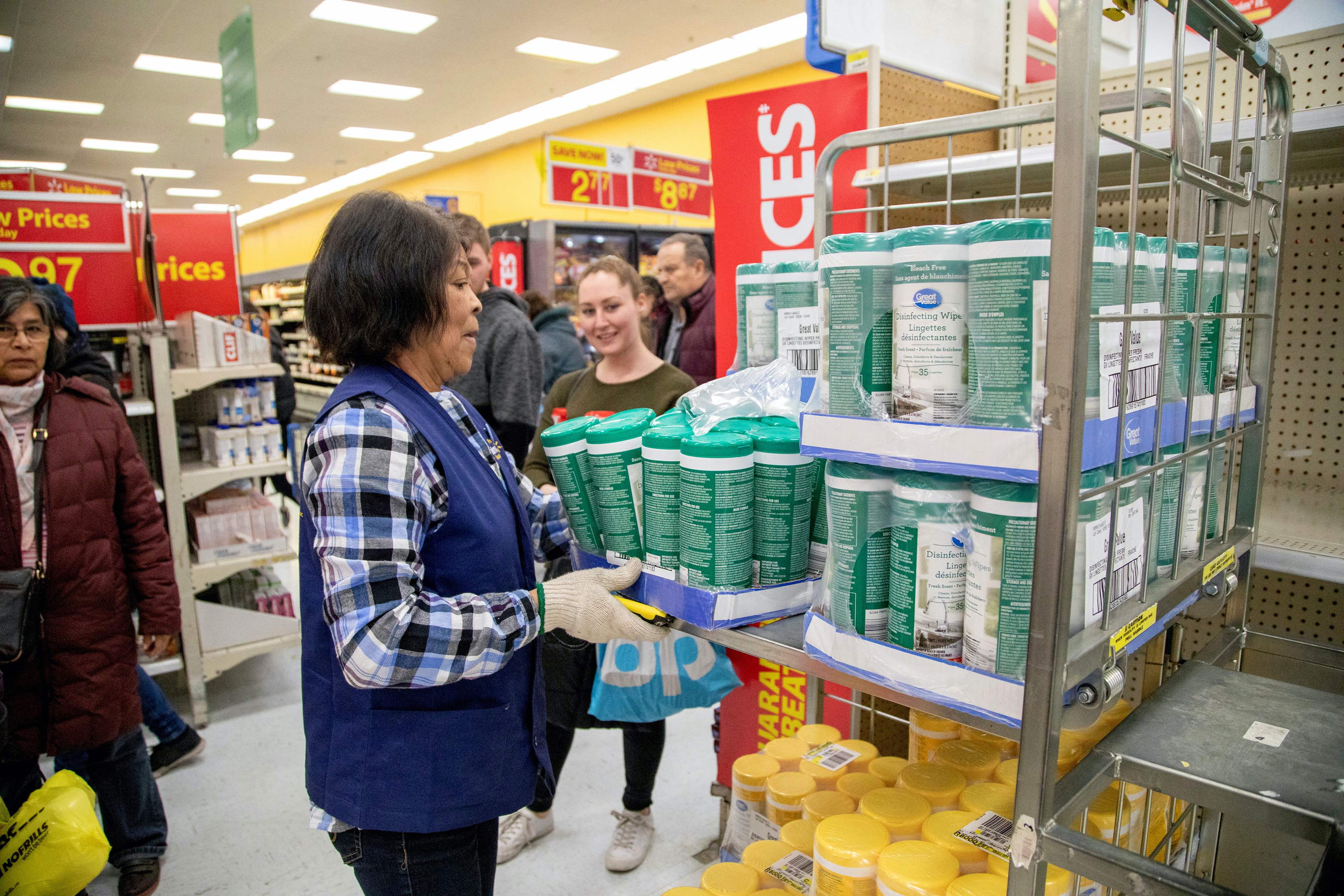People wait as an employee restocks a shelf as people shop at a Walmart Supercentre in Toronto, Ontario, Canada
