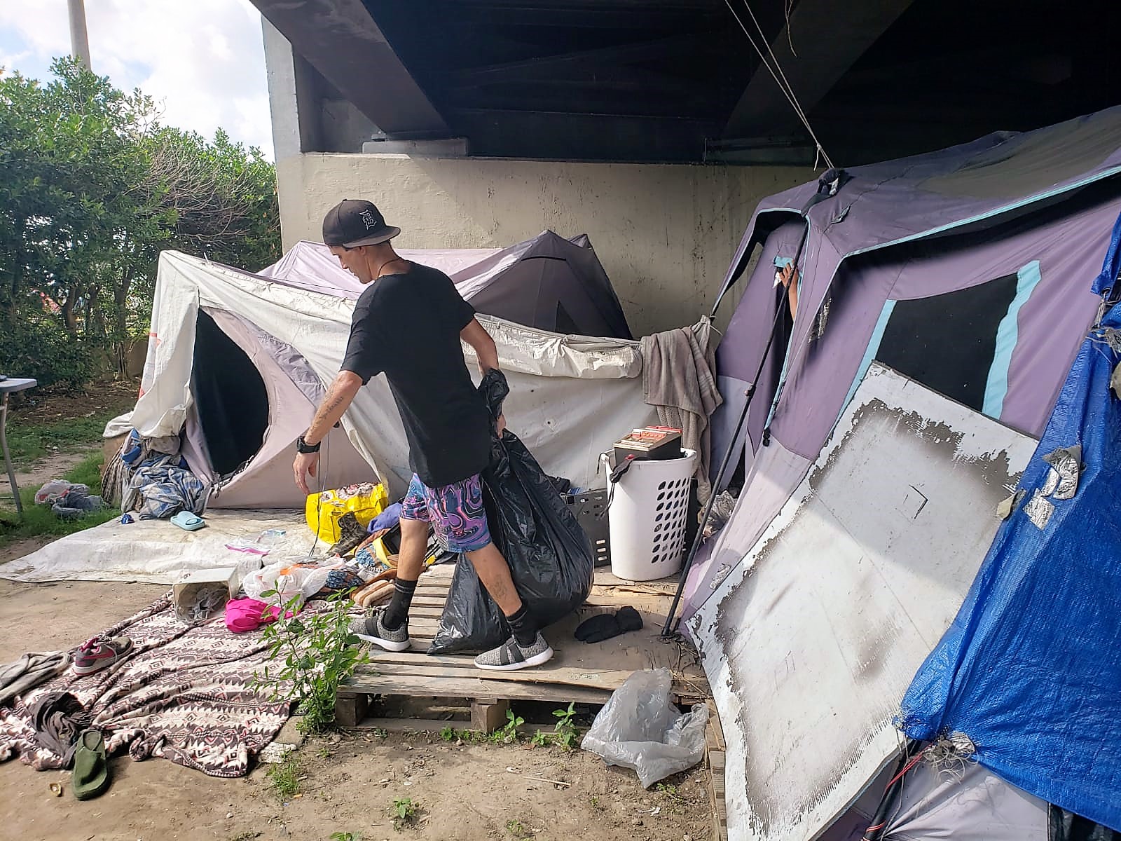 A photo of Terry walking by a tent with a plastic bagl.