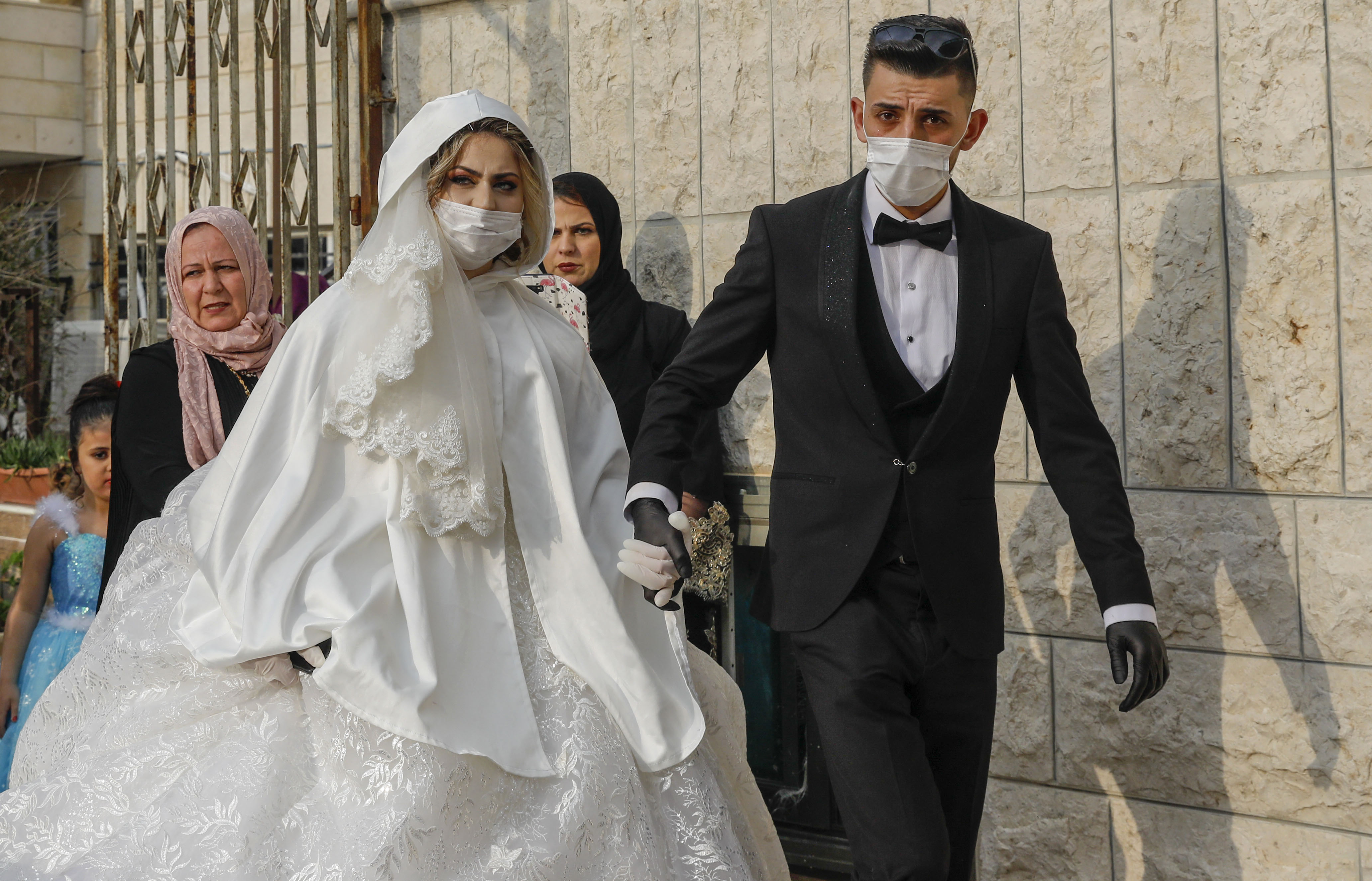 Newly-wed Palestinians Yazen Abu Ramooz (R) and Iman Ghaith, both wearing protective masks during the COVID-19 coronavirus pandemic, walk in the neighbourhood of Beit Hanina in Israeli annexed East Jerusalem, on April 17, 2020. (Photo by