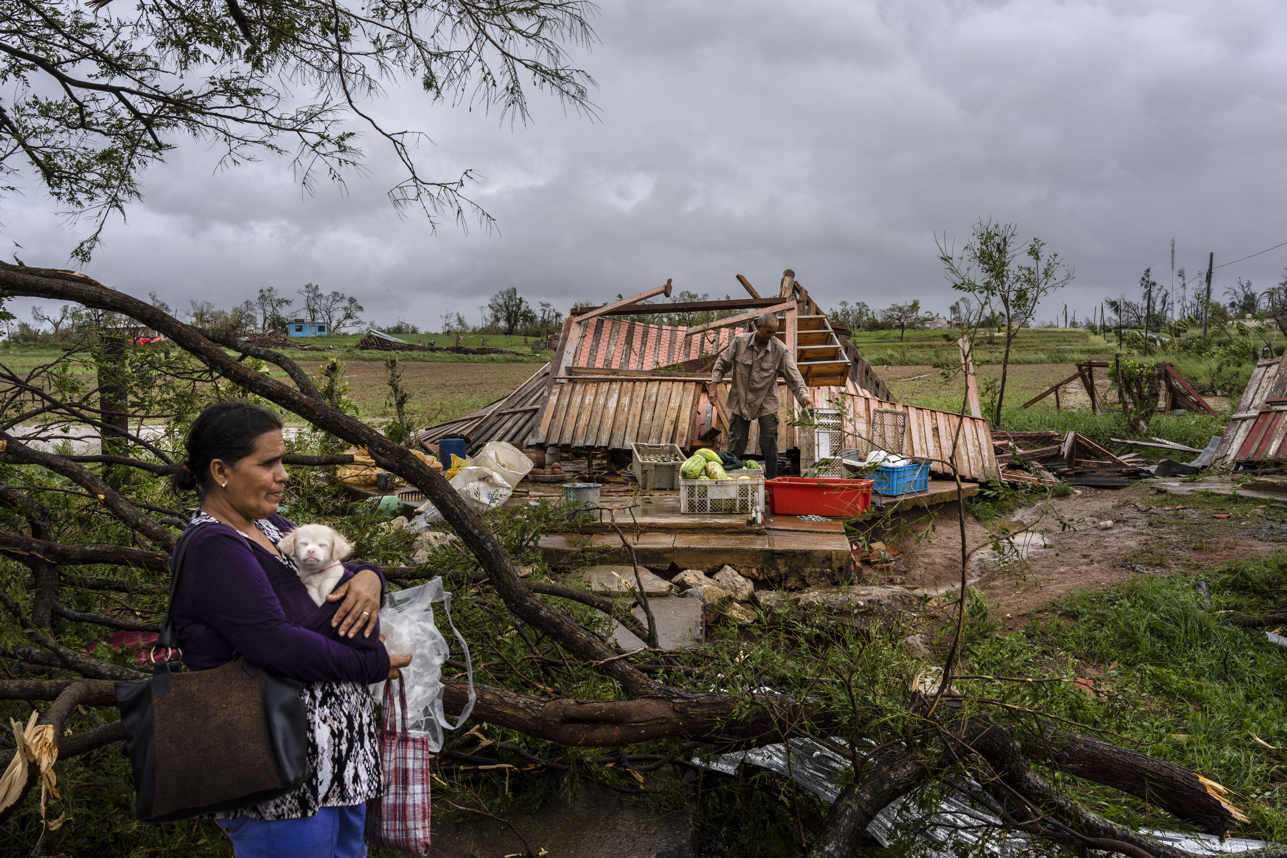 Mercedes Valdez holds her dog Kira as she waits for transportation after Hurricane Ian destroyed her home, whcich lies in ruins behind her