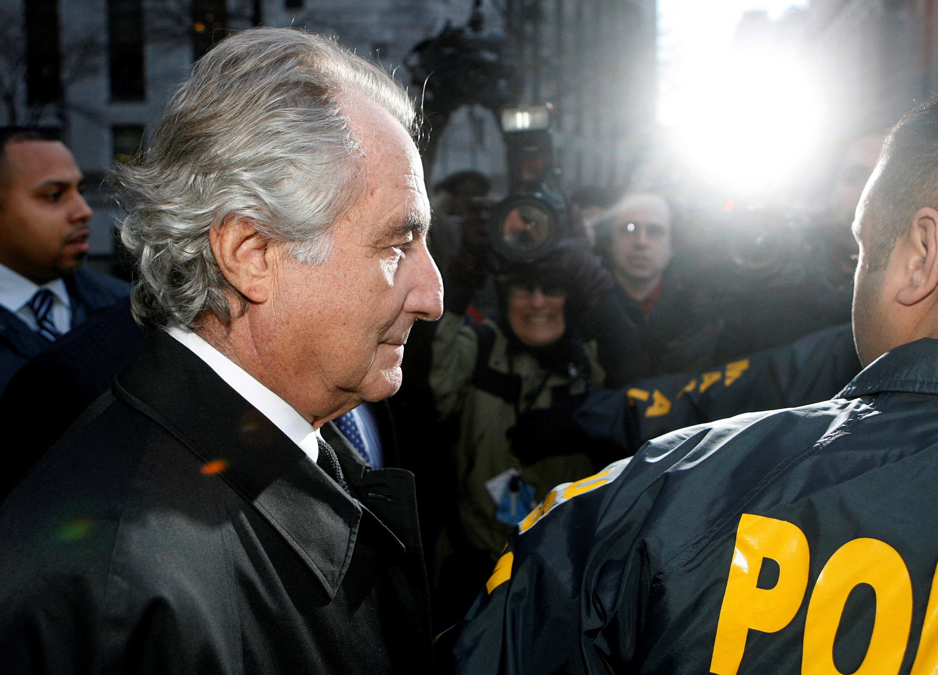 Disgraced financier Bernard Madoff is escorted by police and photographed by the media as he departs U.S. Federal Court after a hearing in New York