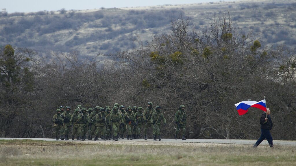 Russian soldiers march as a local resident waves a Russian flag